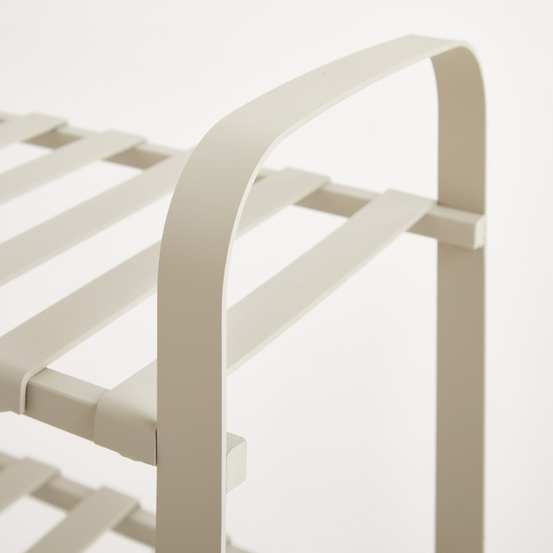 Ein minimalistischer, weißer Metallrahmen mit sich kreuzenden diagonalen Balken vor einem schlichten, hellen Hintergrund.