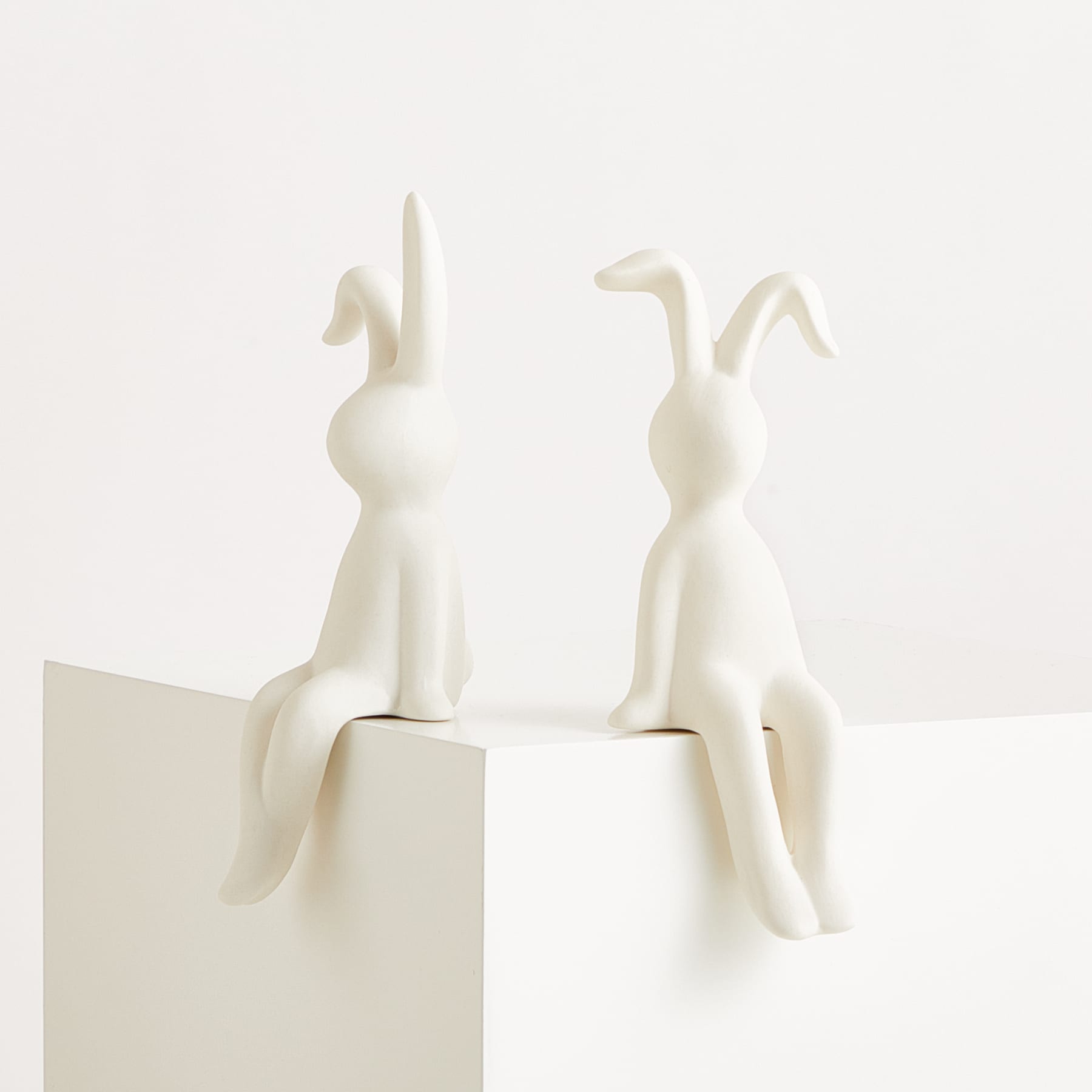 Zwei weiße Keramikfiguren von Kaninchen oder Hasen sitzen auf einem schlichten weißen Hintergrund.