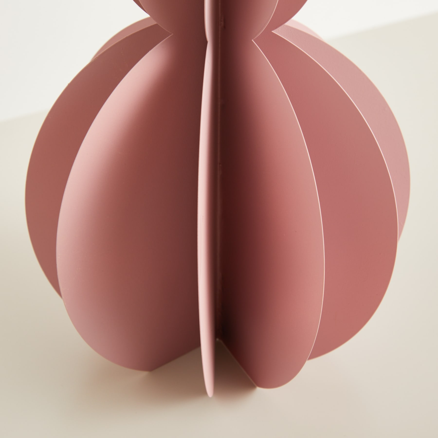 Eine skulpturale, abstrakte Form in einem weichen, gedämpften Rosaton mit überlappenden, geschwungenen Formen, die vor einem neutralen Hintergrund eine optisch beeindruckende und minimalistische Komposition erzeugen.