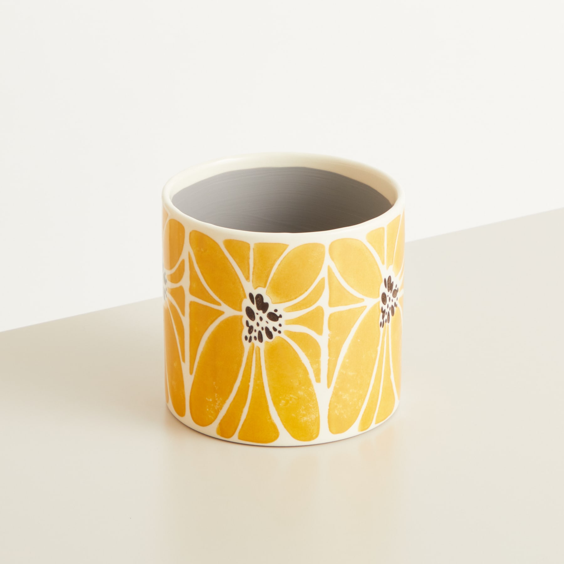 Ein Keramikbecher oder eine Keramiktasse mit einem leuchtend gelben und schwarzen Blumenmuster auf einem schlichten, hellen Hintergrund.