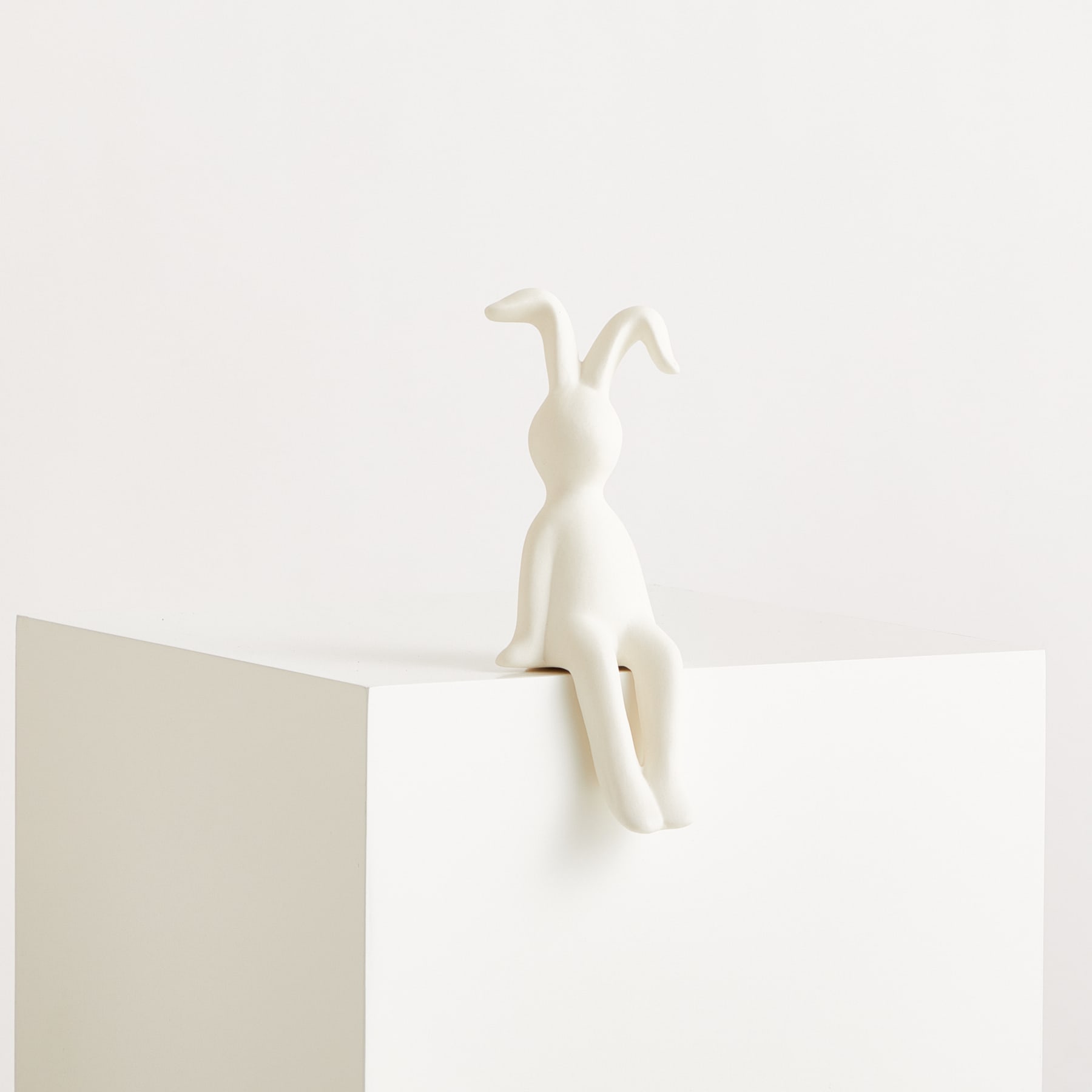 Eine weiße, minimalistische Figur sitzt auf einer weißen Plattform vor einem schlichten, hellen Hintergrund.