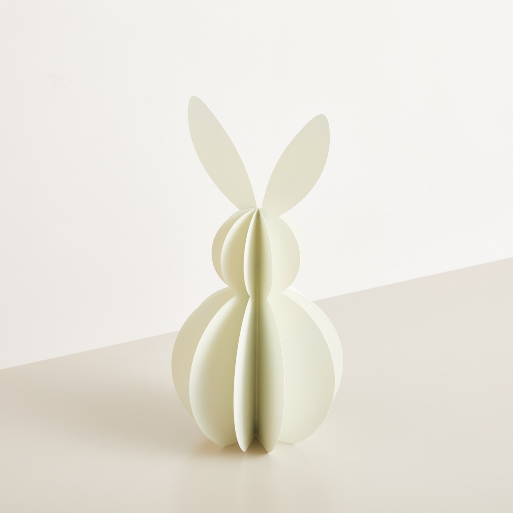 Eine einfache, minimalistische Skulptur einer stilisierten Kaninchen- oder Hasenfigur, bestehend aus glatten, geschwungenen weißen oder cremefarbenen Formen vor einem schlichten, hellen Hintergrund.