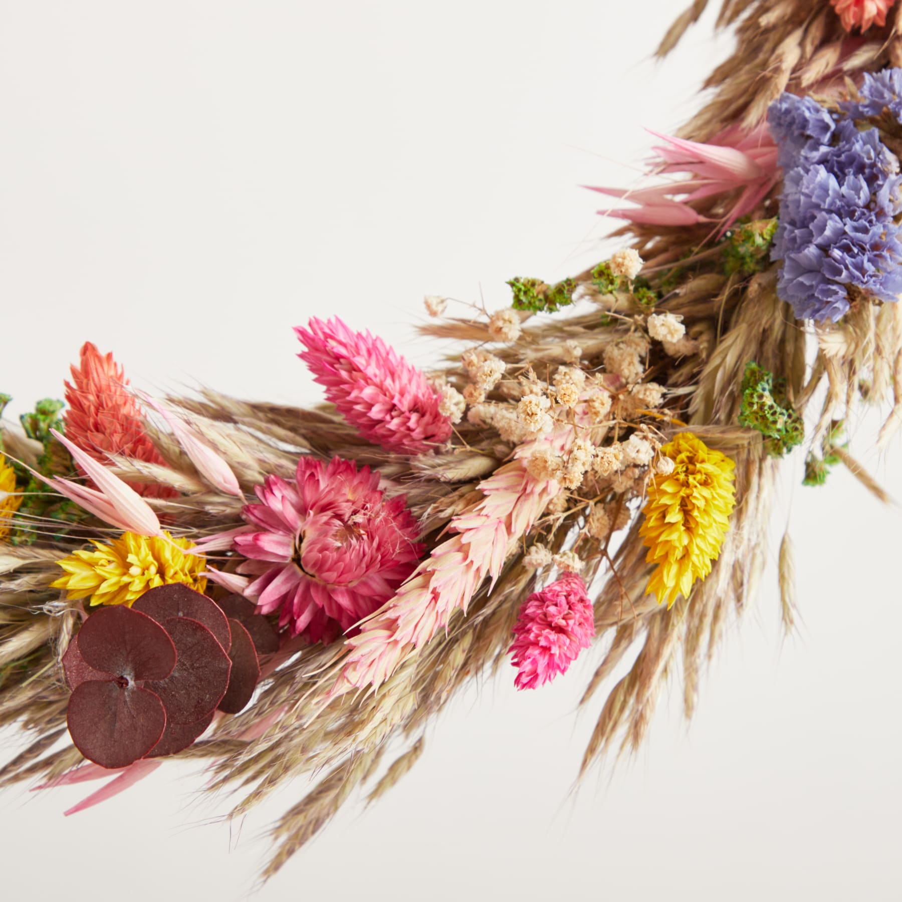 Ein lebendiger Strauß getrockneter Blumen, darunter rosa und violette Chrysanthemen, Weizenhalme und andere natürliche Elemente, vor einem schlichten weißen Hintergrund.