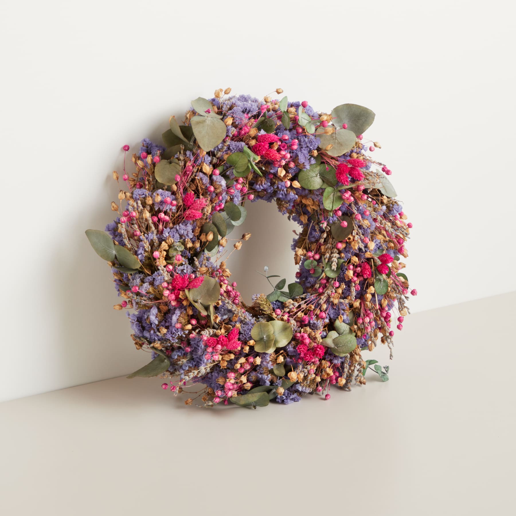 Ein lebendiger und farbenfroher Kranz aus verschiedenen getrockneten Blumen, Beeren und Blättern auf einem schlichten weißen Hintergrund.