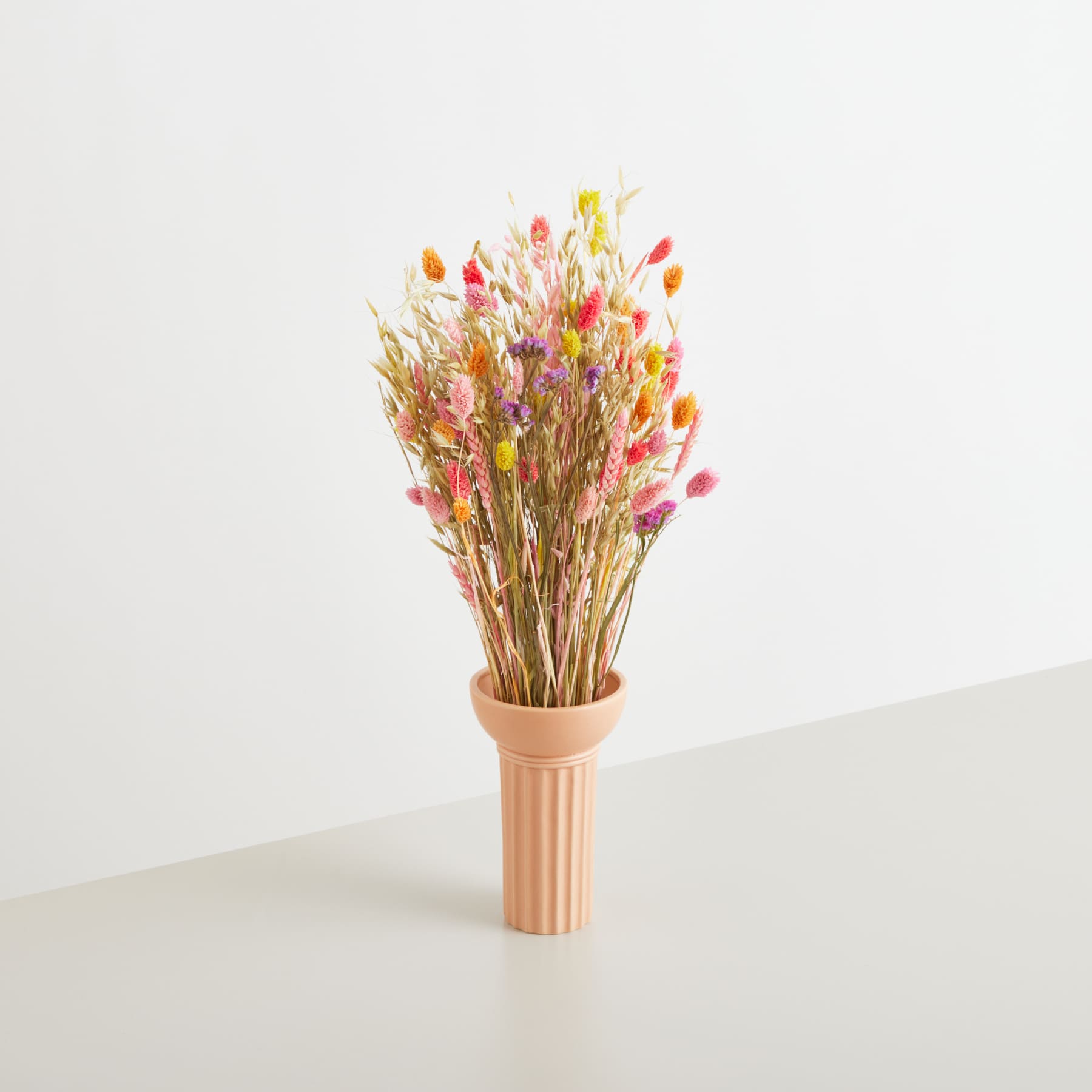 Ein Strauß getrockneter Blumen in einer Terrakottavase steht auf einer schlichten weißen Oberfläche und schafft so eine einfache und natürliche Komposition.