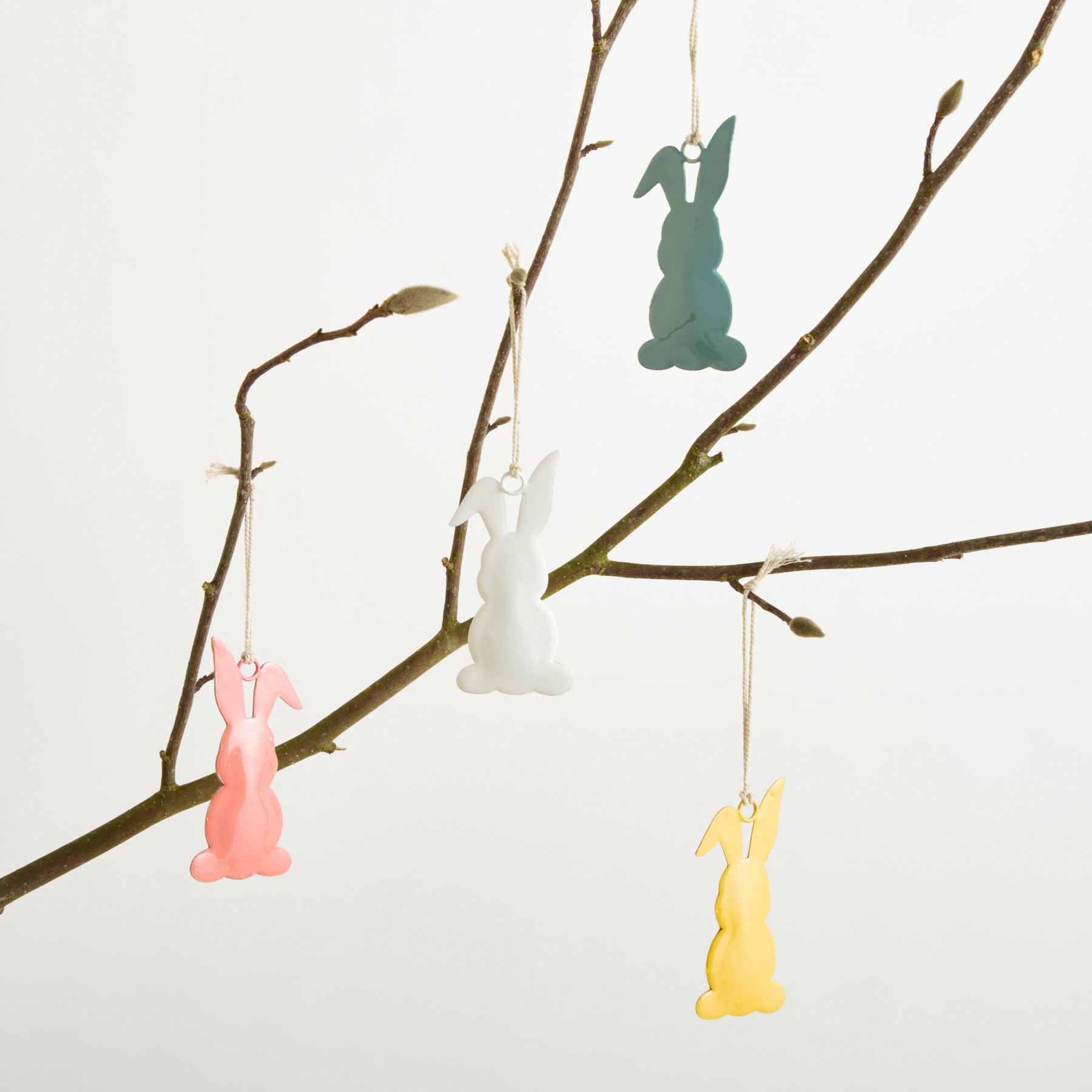 Bunte Hasensilhouetten aus Papier hängen vor einem schlichten weißen Hintergrund von den Zweigen eines kahlen Baumes.