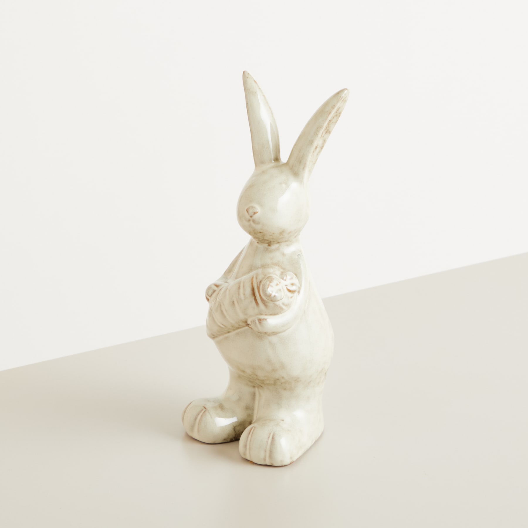 Eine weiße Keramikfigur eines Kaninchens, das aufrecht mit langen Ohren vor einem schlichten weißen Hintergrund steht.