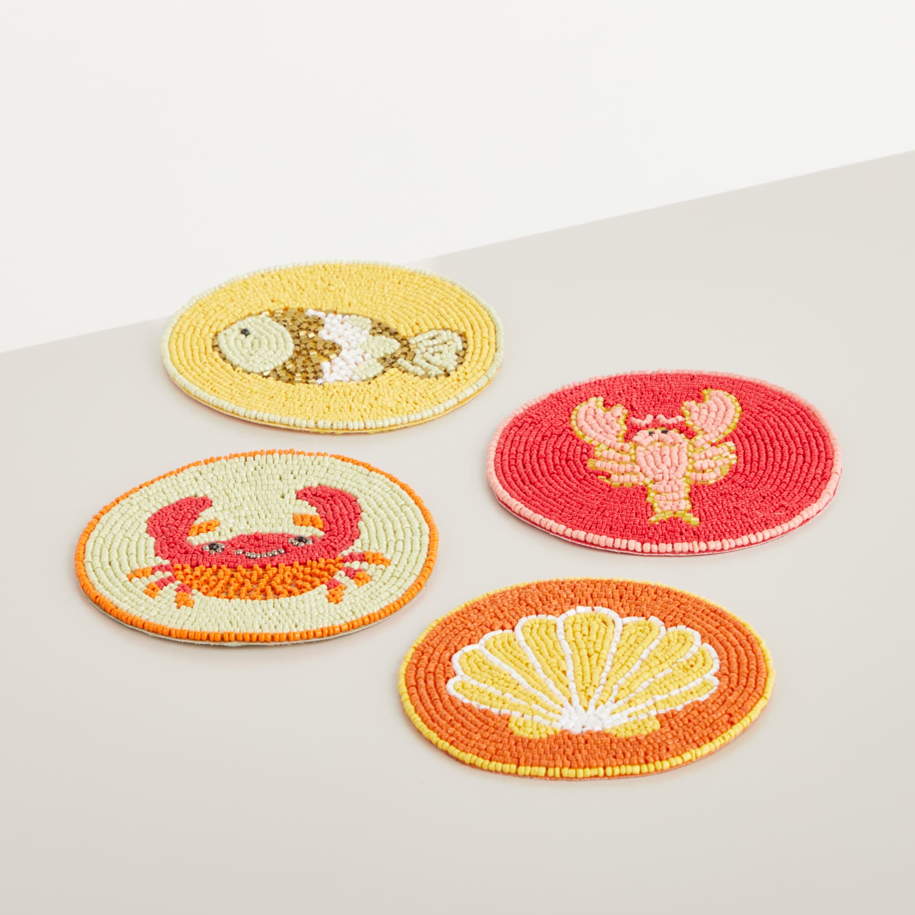 Vier bunte, bestickte Aufnäher mit der Darstellung verschiedener Meerestiere und Symbole, darunter ein Fisch, eine Krabbe und eine Muschel, sind auf einer schlichten, hellen Oberfläche angeordnet.