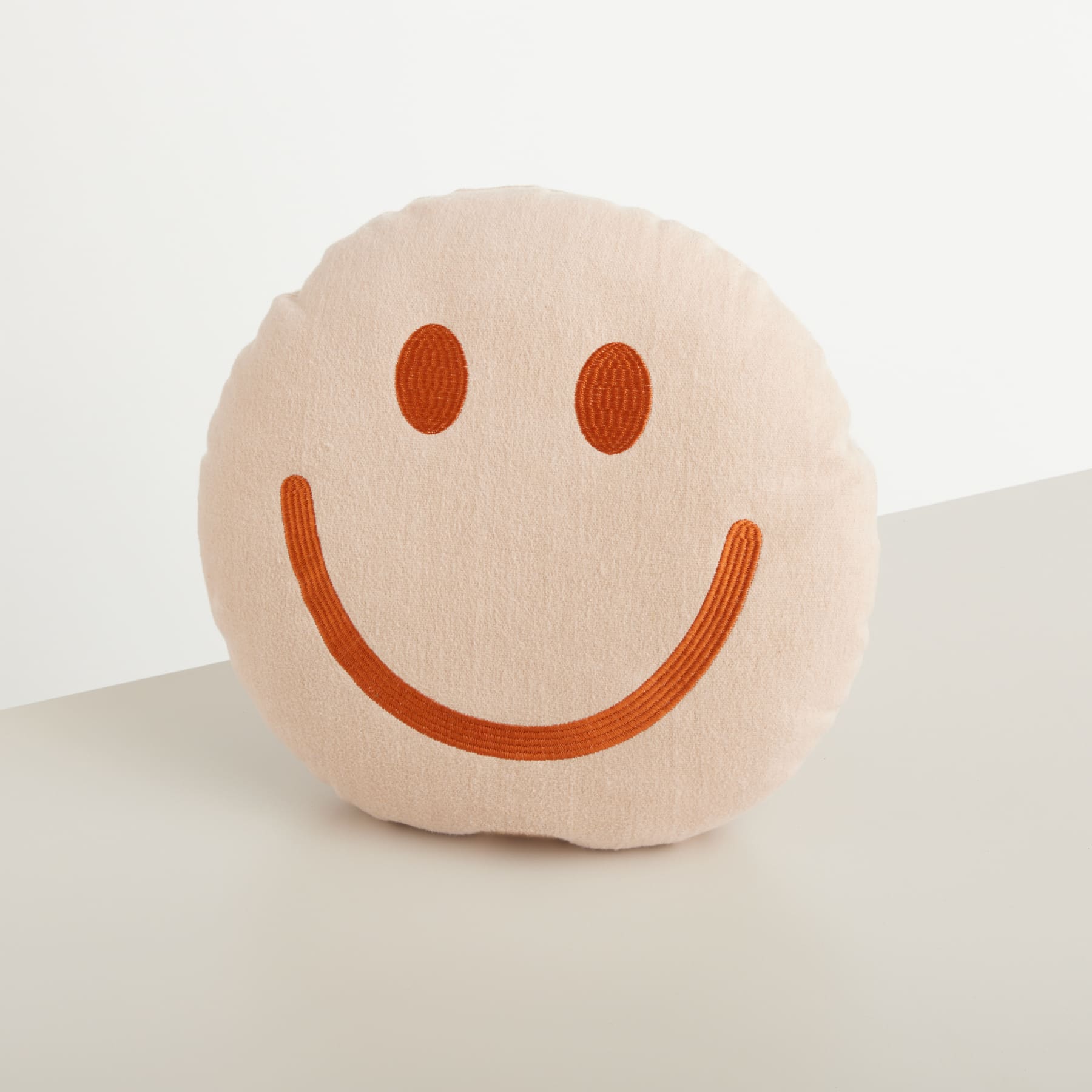 Ein weiches, plüschiges, rundes Kissen mit einem fröhlichen, orangefarbenen Smiley-Gesicht, das auf einem schlichten weißen Hintergrund ruht.