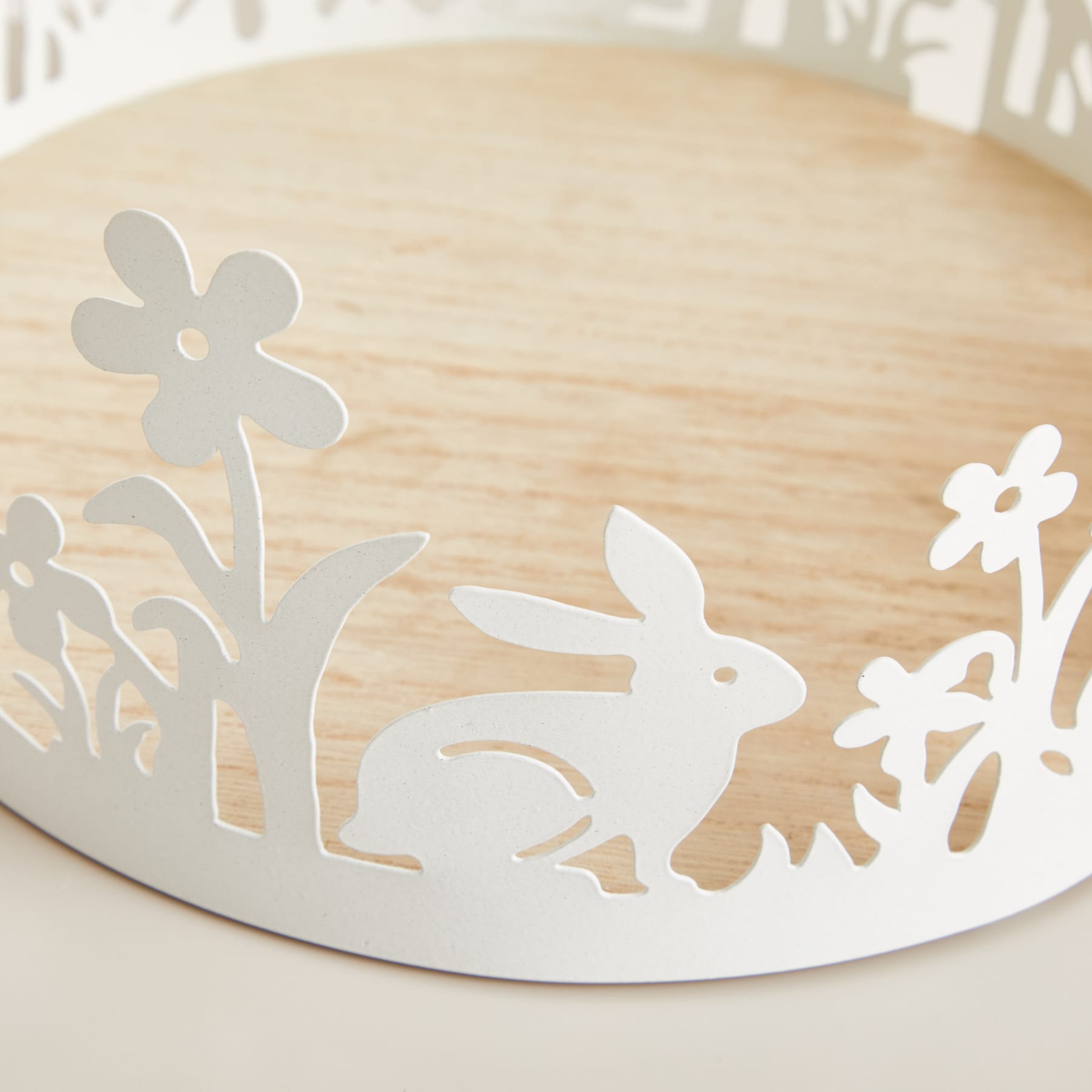 Ein Holztablett mit einem lasergeschnittenen Design mit einem Kaninchen und Blumen vor hellem Hintergrund.