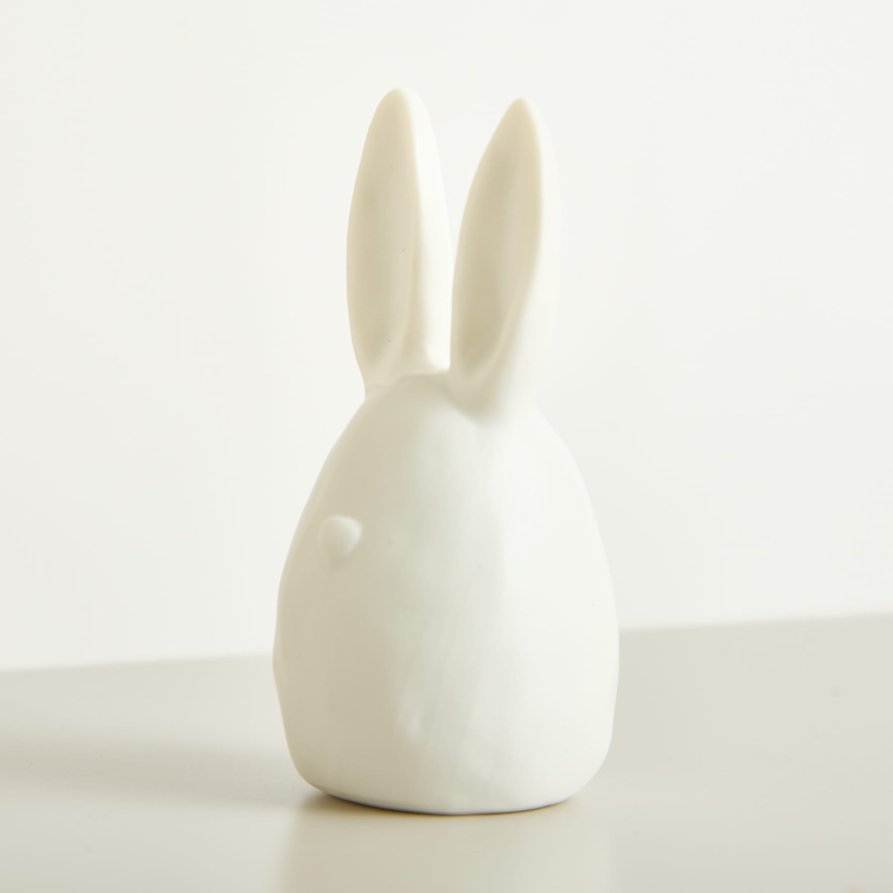 Eine einfache, minimalistische weiße Kaninchenfigur aus Keramik steht allein auf einem schlichten weißen Hintergrund.