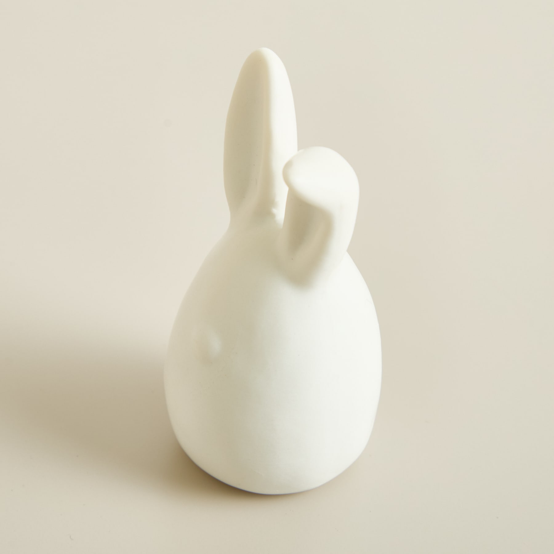 Eine einfache, minimalistische weiße Keramikfigur eines Kaninchens oder Hasen steht vor einem schlichten, hellen Hintergrund.