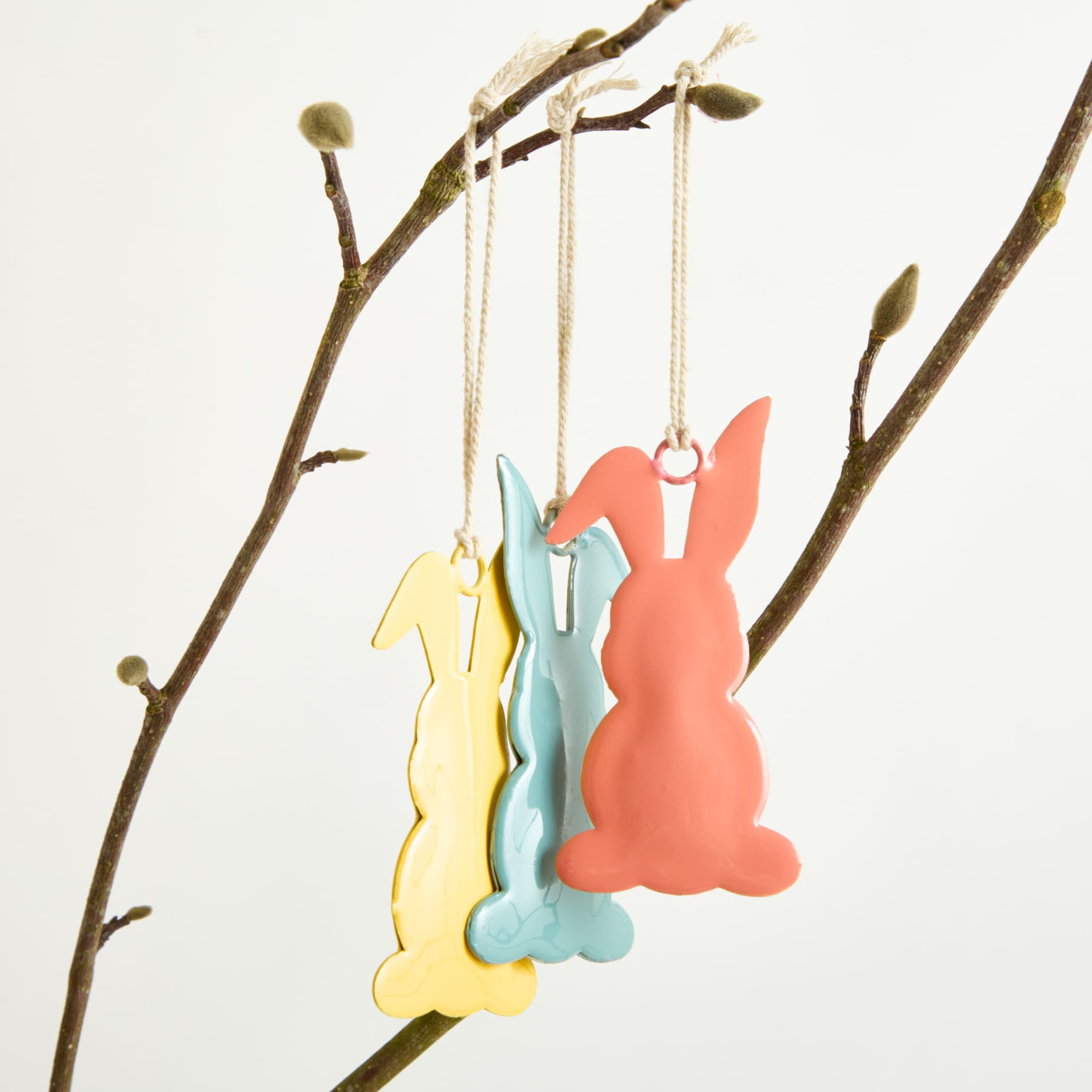 Bunte Osterhasenfiguren aus Holz hängen an einem Zweig mit Knospen und sorgen für eine skurrile und festliche Atmosphäre.