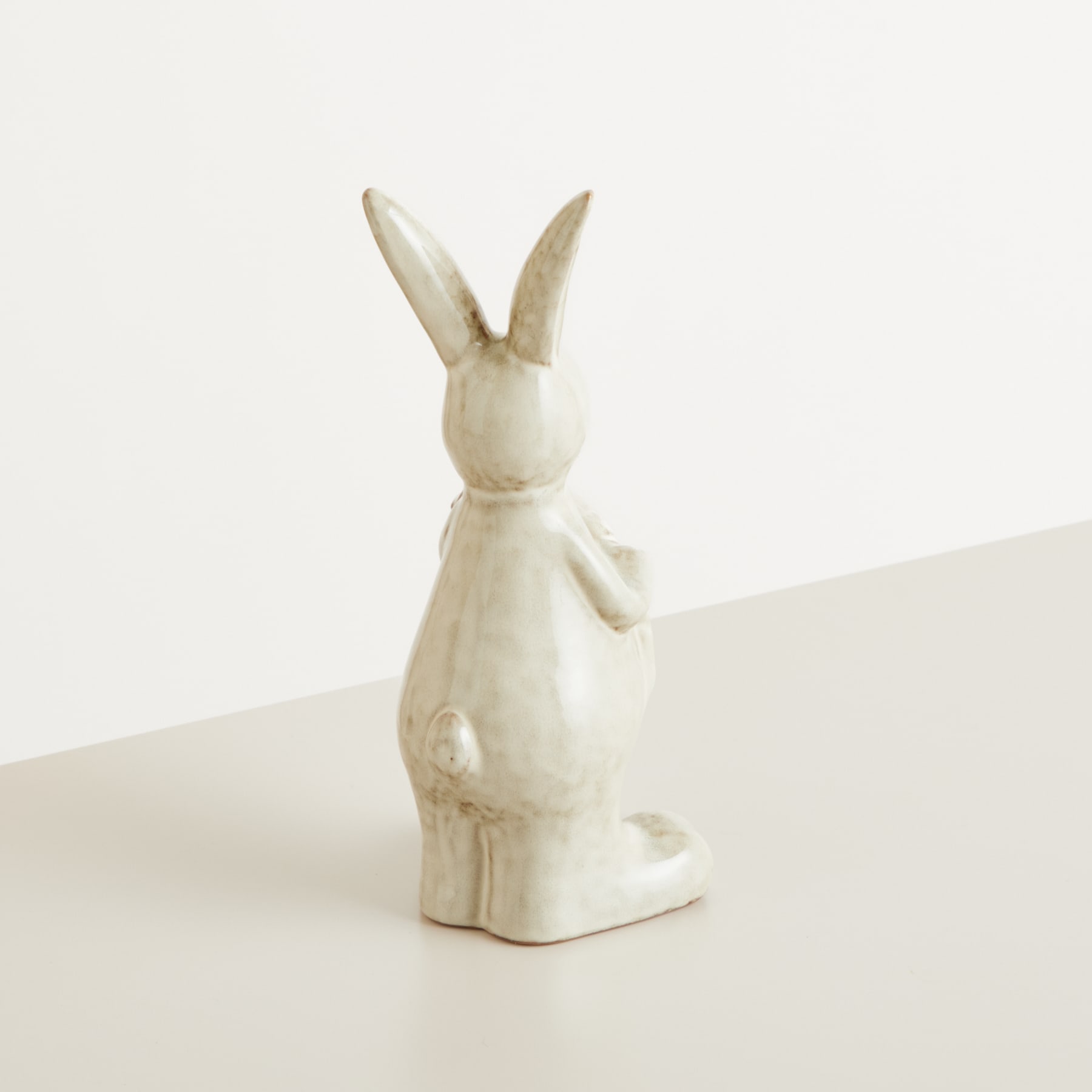 Eine weiße Keramikfigur eines Kaninchens oder Hasen steht auf einer schlichten, hellen Oberfläche vor einem schlichten, hellen Hintergrund.