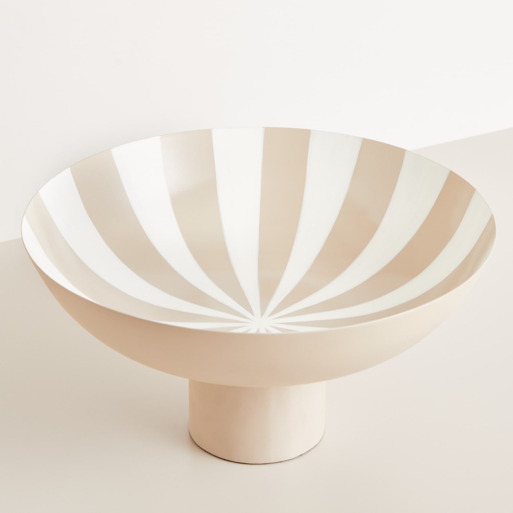 Auf einem schlichten, hellen Hintergrund steht ein beige-weiß gestreiftes, schalenförmiges Objekt.