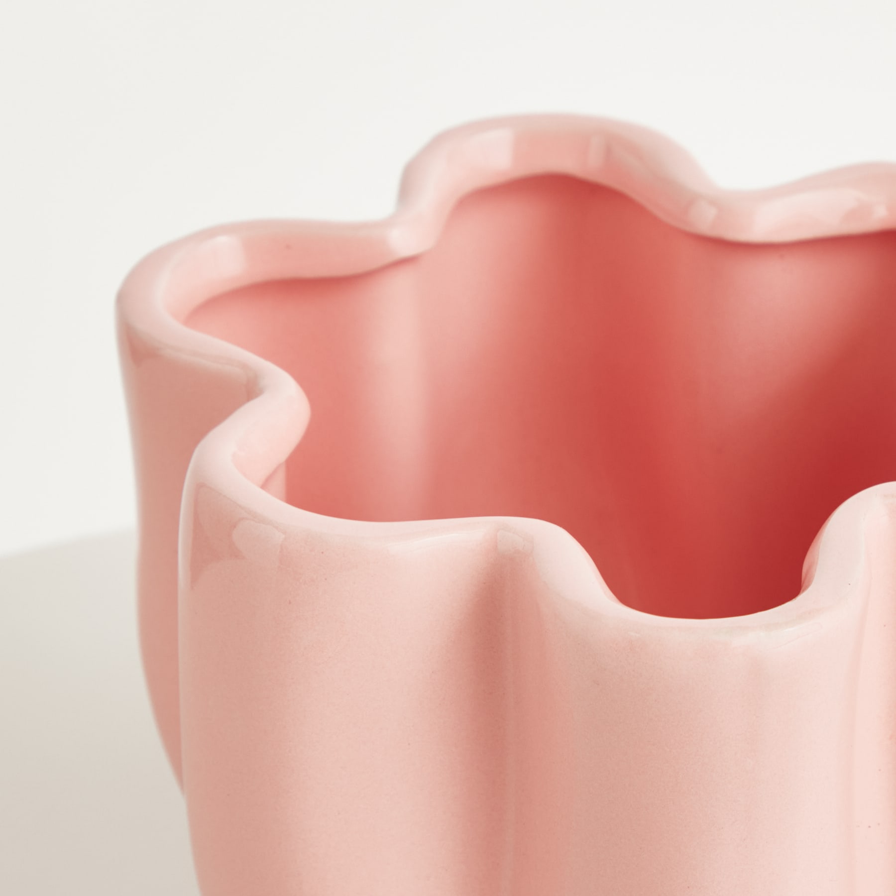 Ein leuchtendes, welliges rosa Keramikgefäß mit einer weichen, organischen Form steht vor einem schlichten weißen Hintergrund und schafft eine optisch beeindruckende und minimalistische Komposition.