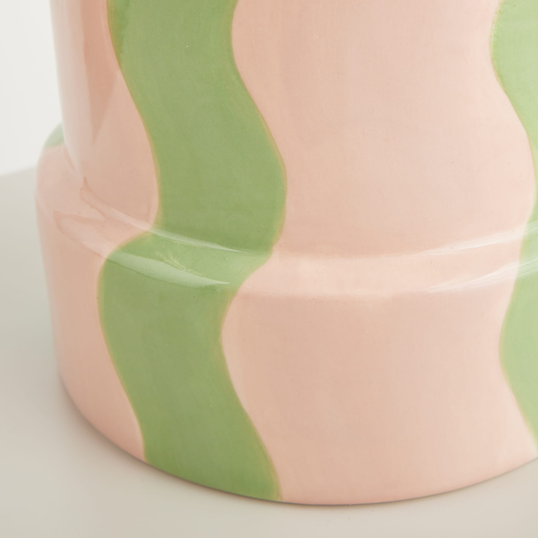 Eine Vase oder ein Behälter aus Keramik in sanften Pastellrosa- und Grüntönen mit glatten, geschwungenen Linien und minimalistischem, abstraktem Design.