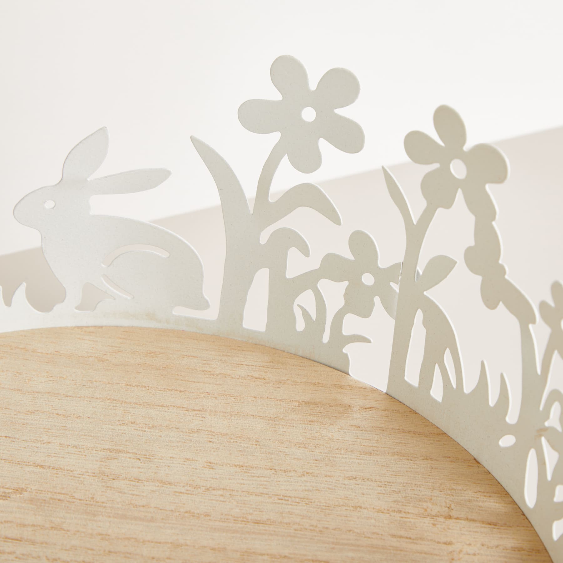 Das Bild zeigt eine Holzoberfläche mit einem Silhouettenmuster aus Kaninchen und Blumen im Vordergrund, vor einem schlichten, hellen Hintergrund.