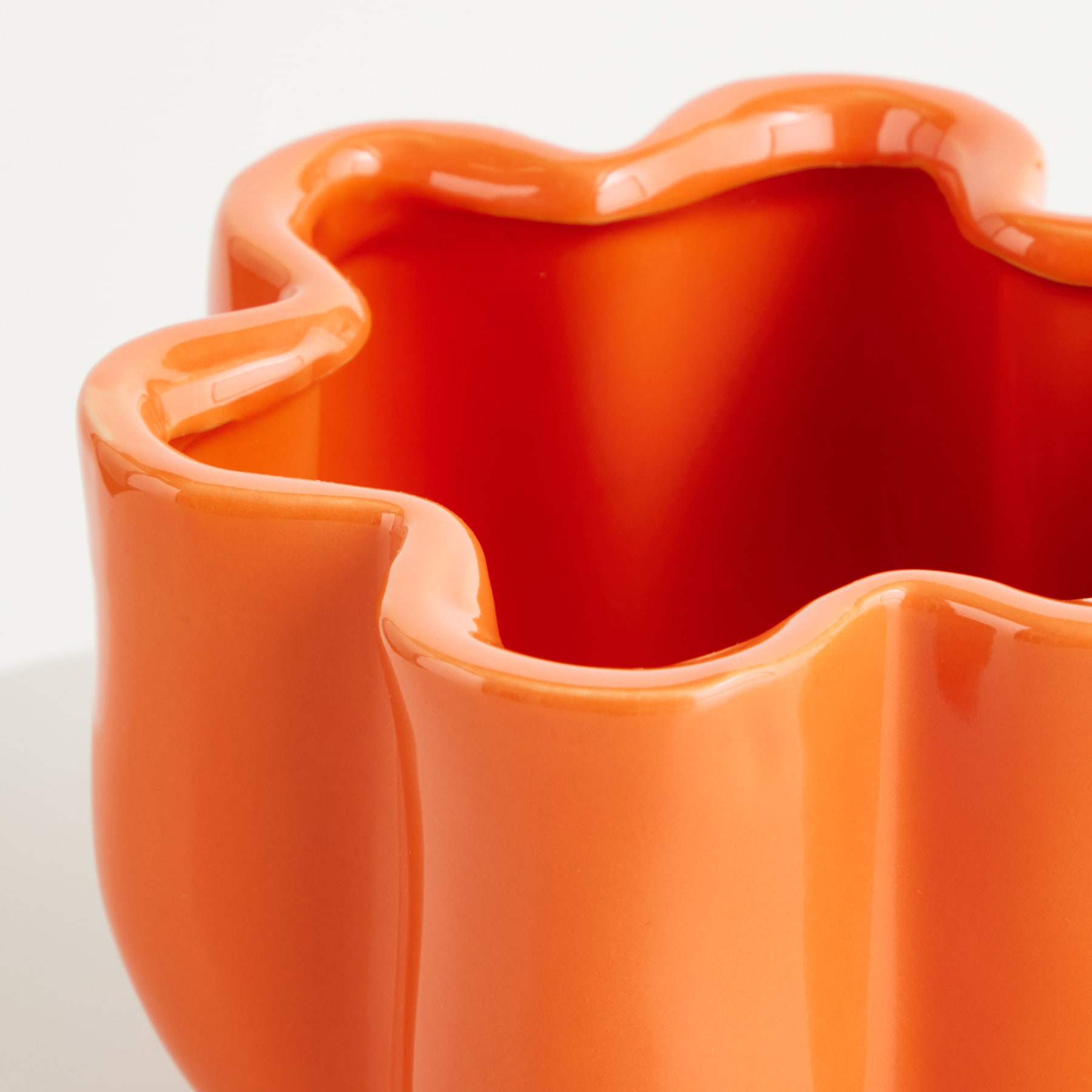 Eine leuchtend orangefarbene Keramikvase oder -schale in Wellenform vor einem schlichten weißen Hintergrund.