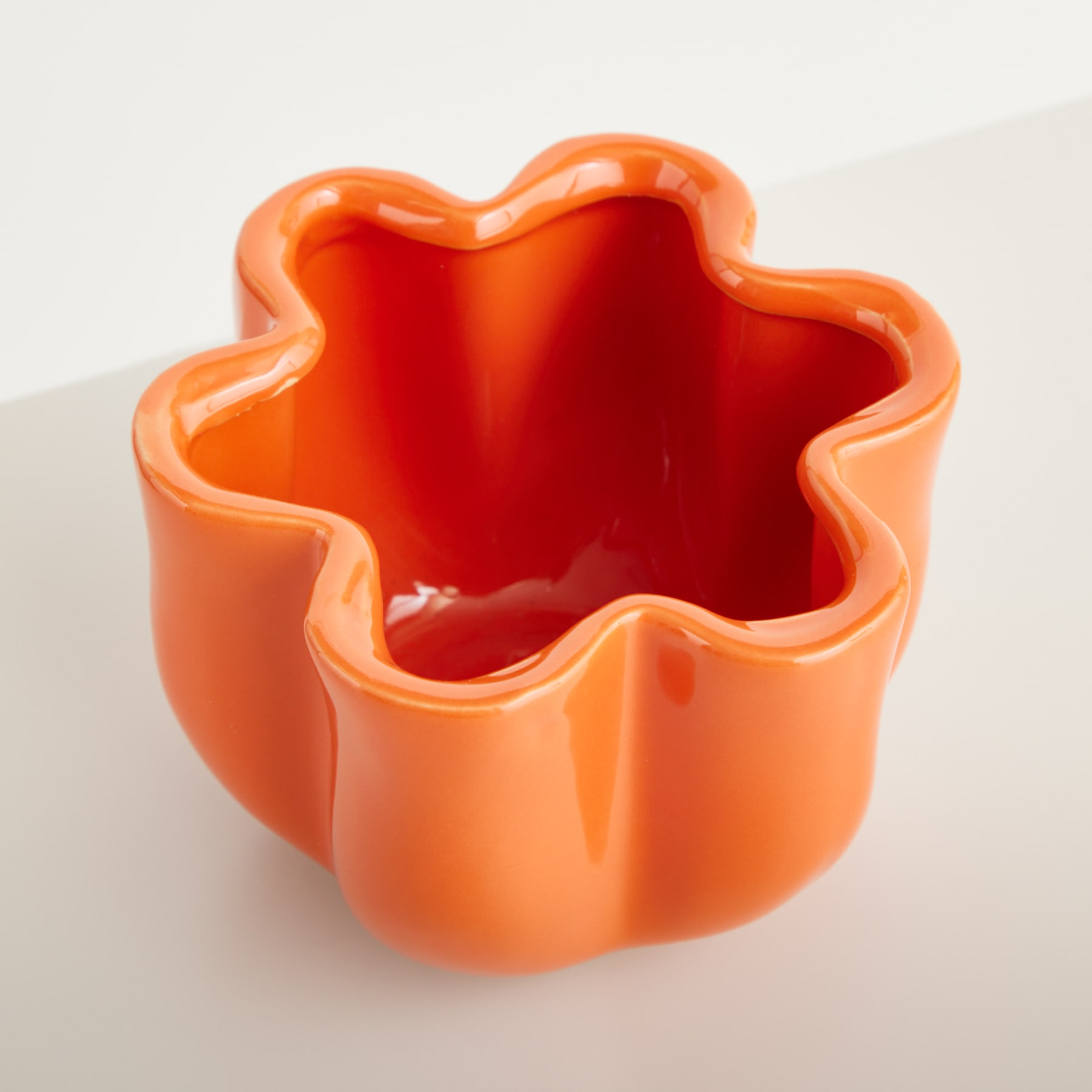 Auf einem schlichten weißen Hintergrund steht ein leuchtend orangefarbener Keramikbehälter in Sternform.