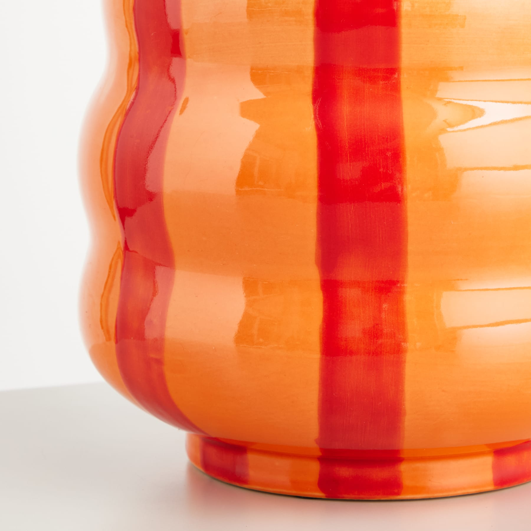 Eine lebendige, abstrakte Glasvase mit kräftigen, überlappenden Streifen in Orange- und Rottönen auf einem schlichten, weißen Hintergrund.