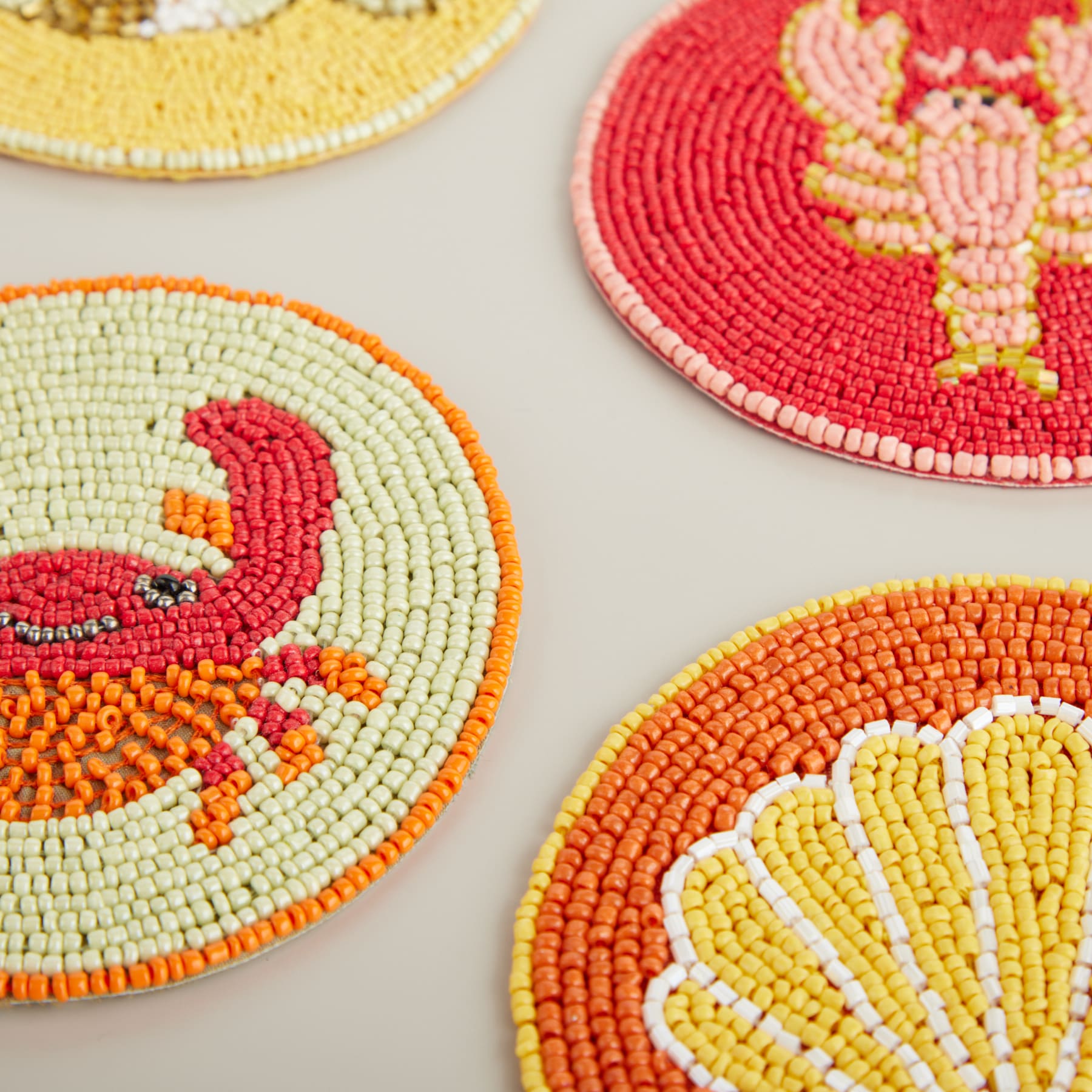 Bunte Untersetzer oder Tischsets aus Perlen mit lebendigen Vogel- und Blumenmustern auf einer hellen Oberfläche.