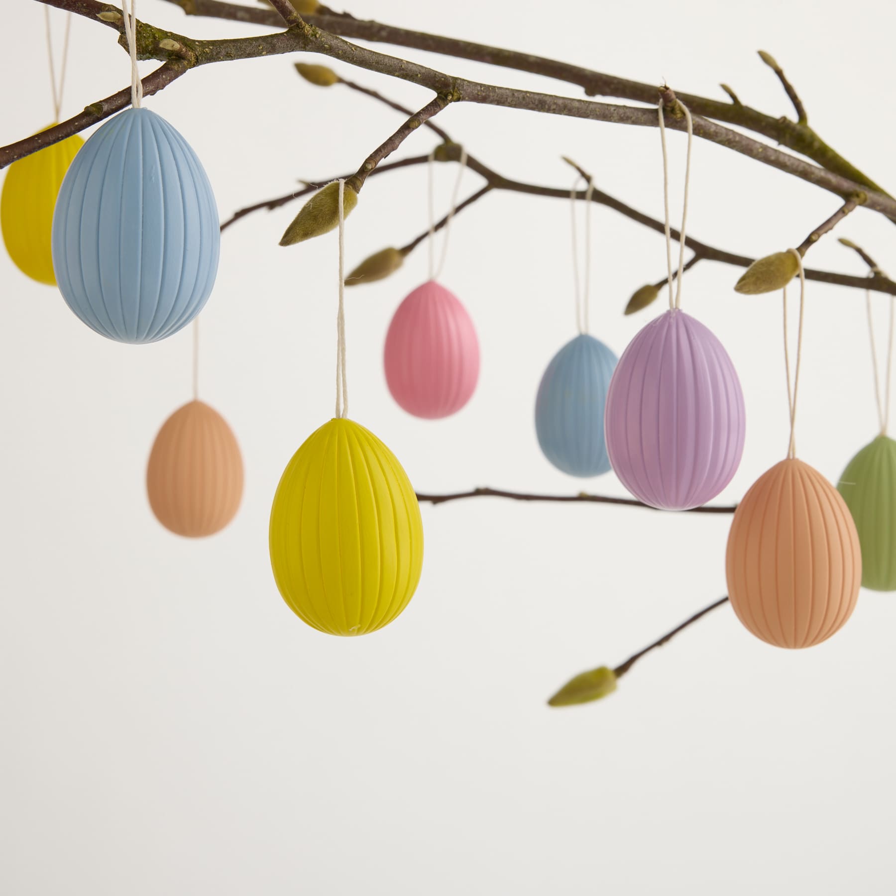 Bunte Ostereier in verschiedenen Pastelltönen hängen von den Zweigen eines Baumes und sorgen für ein skurril-festliches Ambiente.
