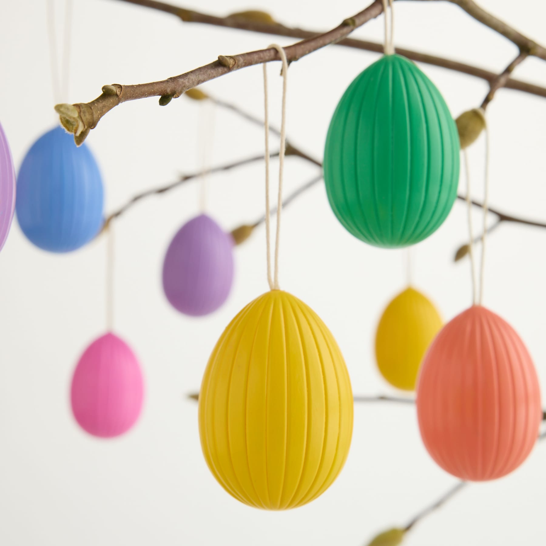 Bunte Ostereier aus Papier hängen vor einem schlichten weißen Hintergrund an einem Ast.