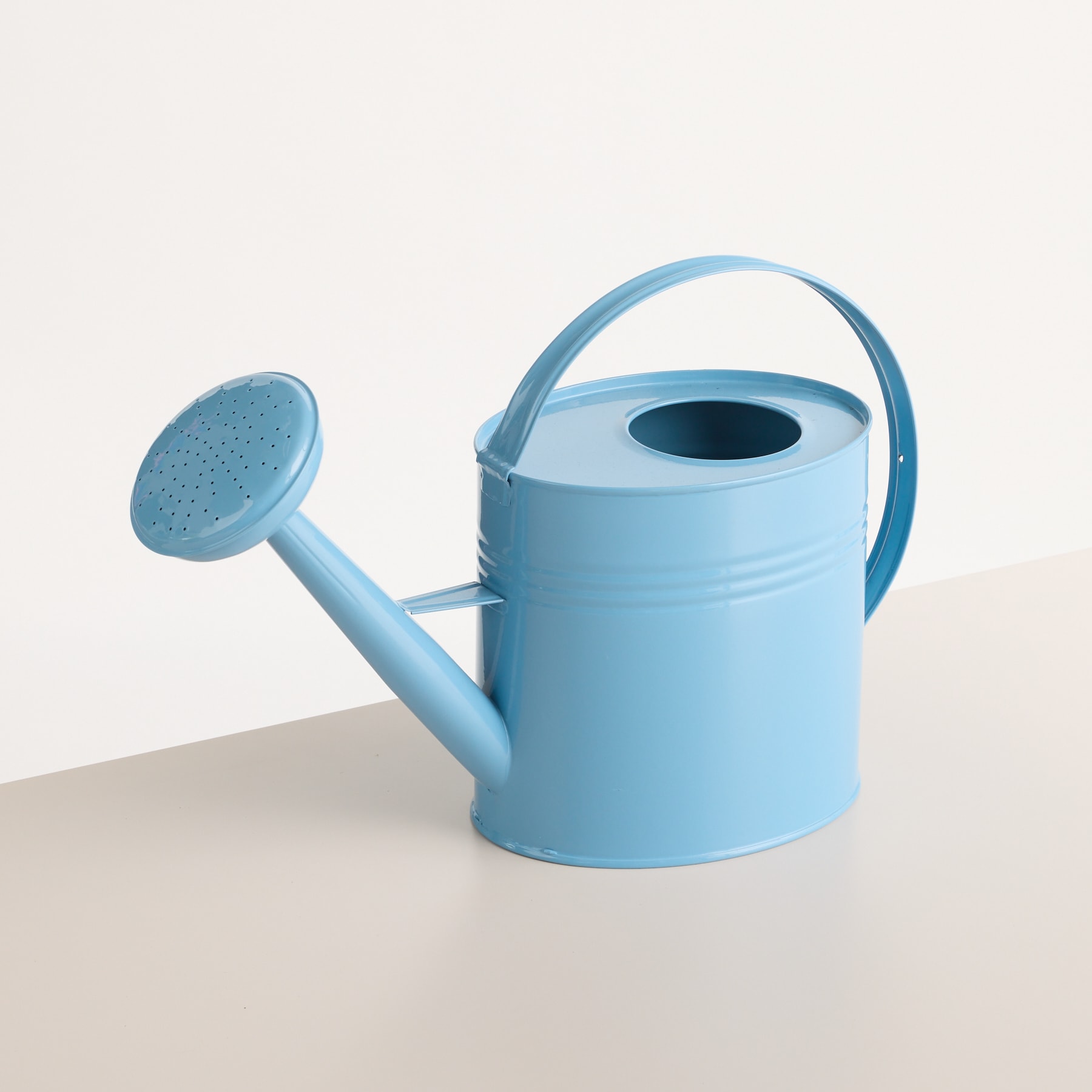 Eine hellblaue Gießkanne steht auf einer schlichten weißen Oberfläche und ihr einfaches und minimalistisches Design hebt sich vom neutralen Hintergrund ab.