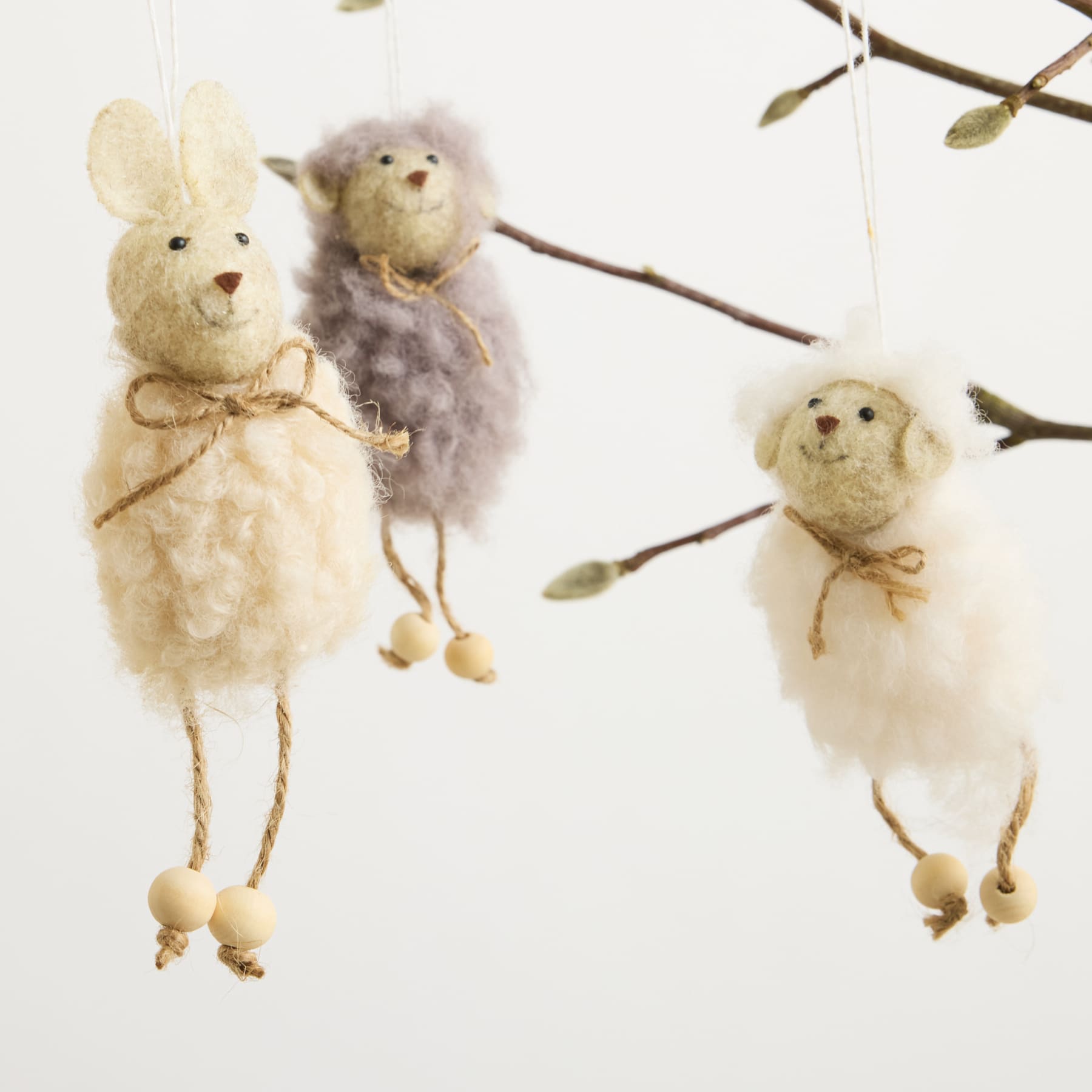 Flauschige, skurrile Plüschfiguren von Kaninchen und Küken hängen vor einem schlichten Hintergrund von Ästen.