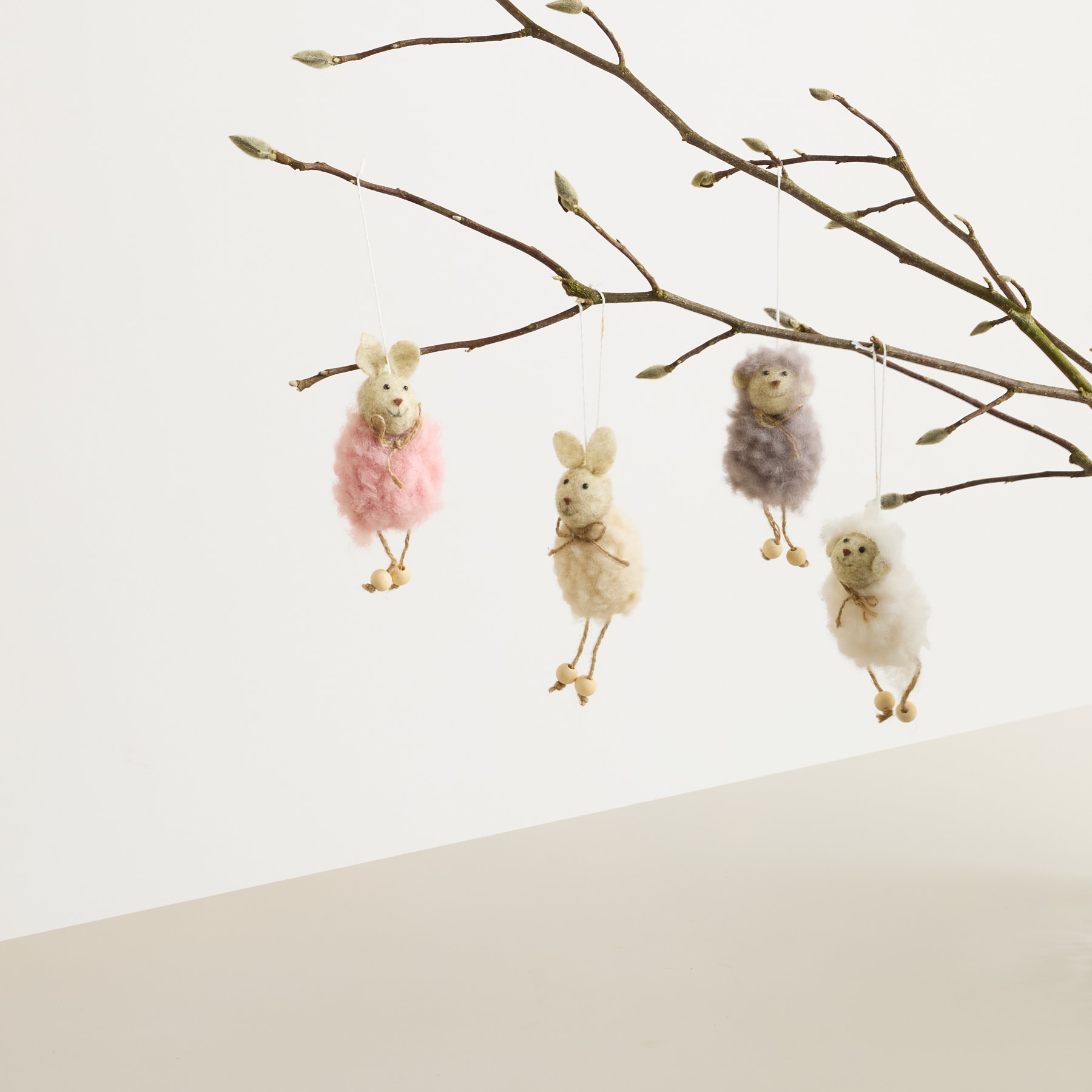 Flauschige Küken in pastellfarbenen Outfits hängen vor einem schlichten weißen Hintergrund von den Zweigen eines kahlen Baumes.