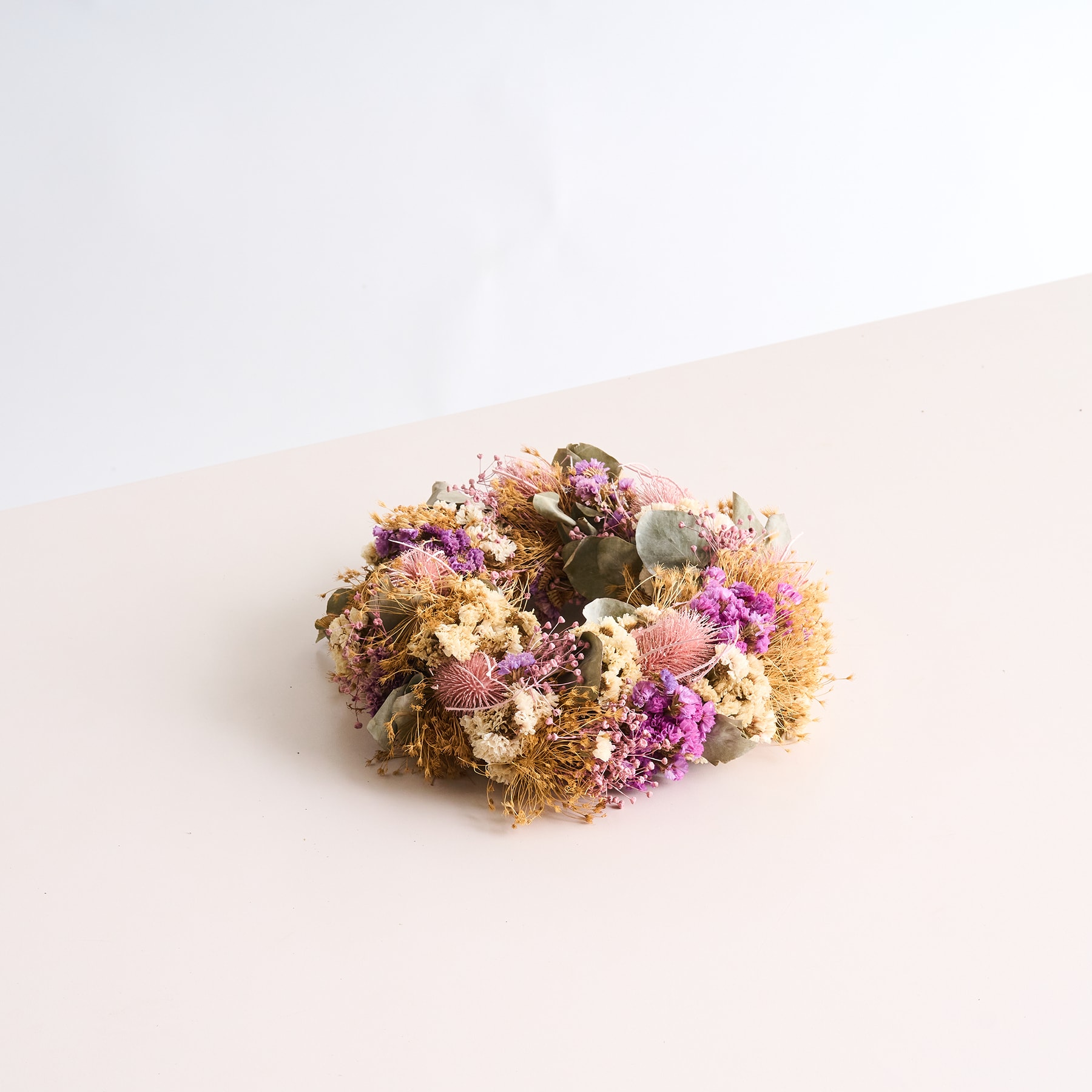 Auf einer schlichten, hellen Oberfläche befindet sich ein farbenfrohes Arrangement aus getrockneten Blumen und Blättern.