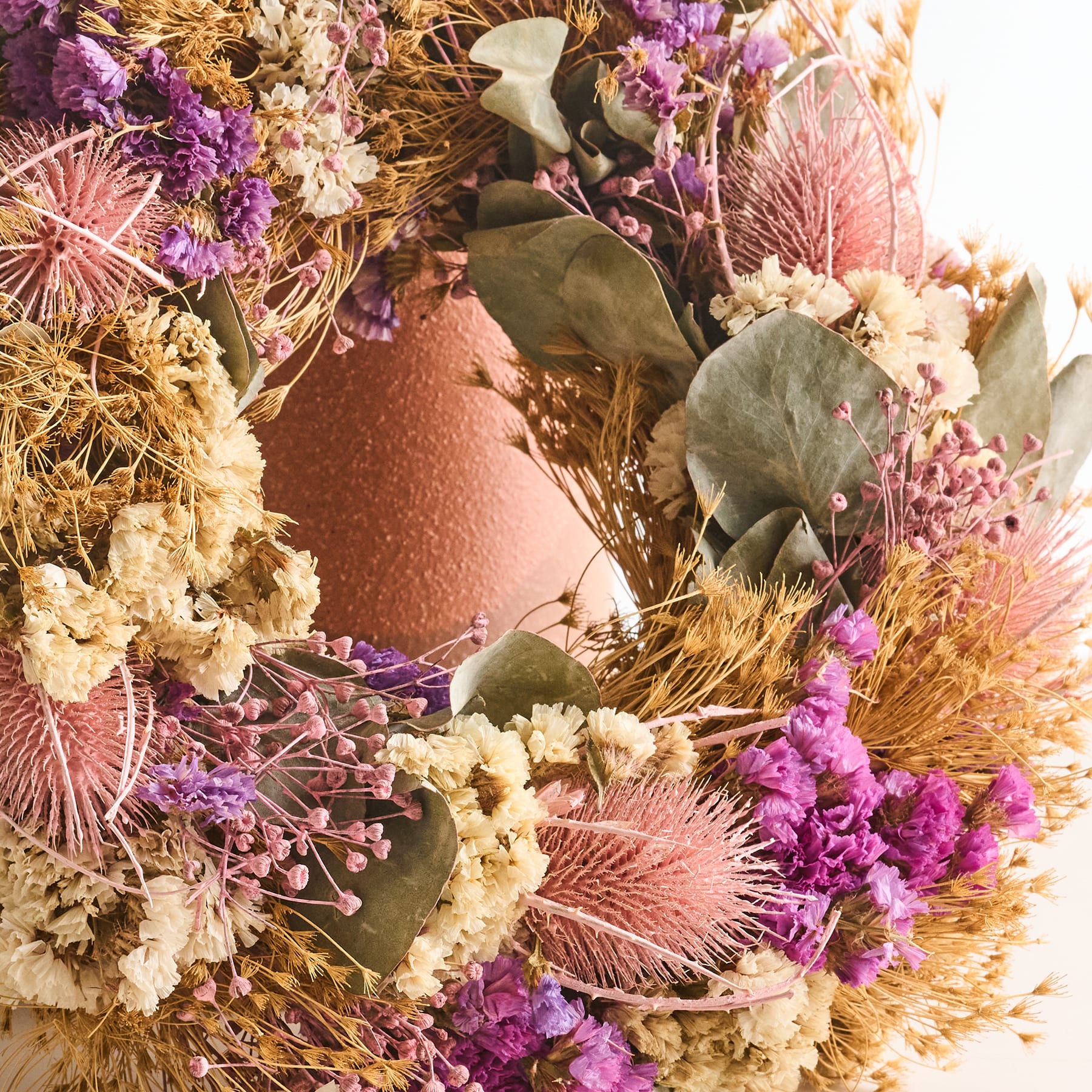 Ein lebendiges und komplexes Blumenarrangement mit einer Vielzahl getrockneter und konservierter Blumen, Blätter und anderer natürlicher Elemente in warmen Erdtönen, die eine optisch fesselnde und strukturierte Komposition ergeben.