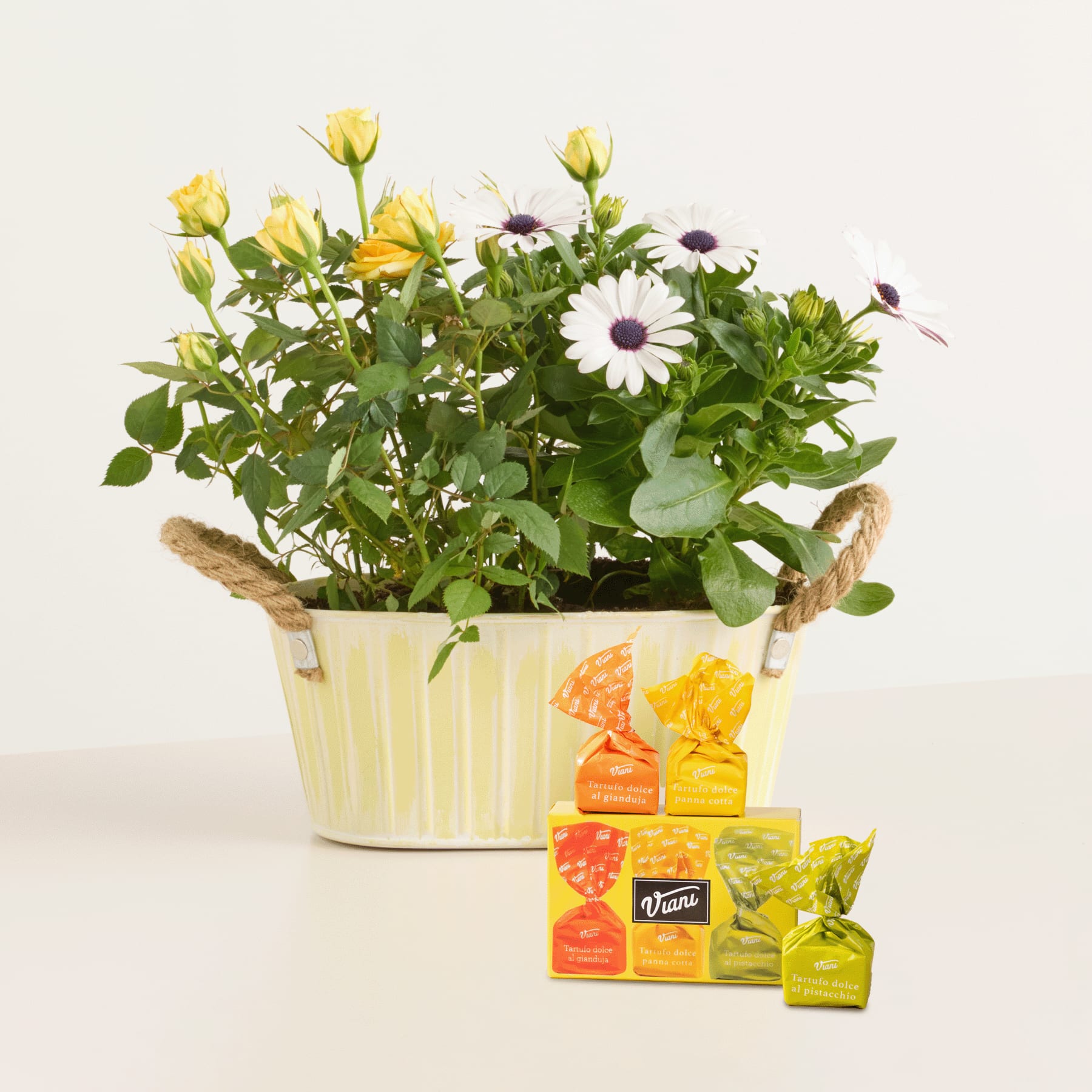 Ein bunter Strauß gelber Rosen und weißer Gänseblümchen in einem dekorativen Blumentopf, im Hintergrund verschiedene Saftkartons der Marke Verna.