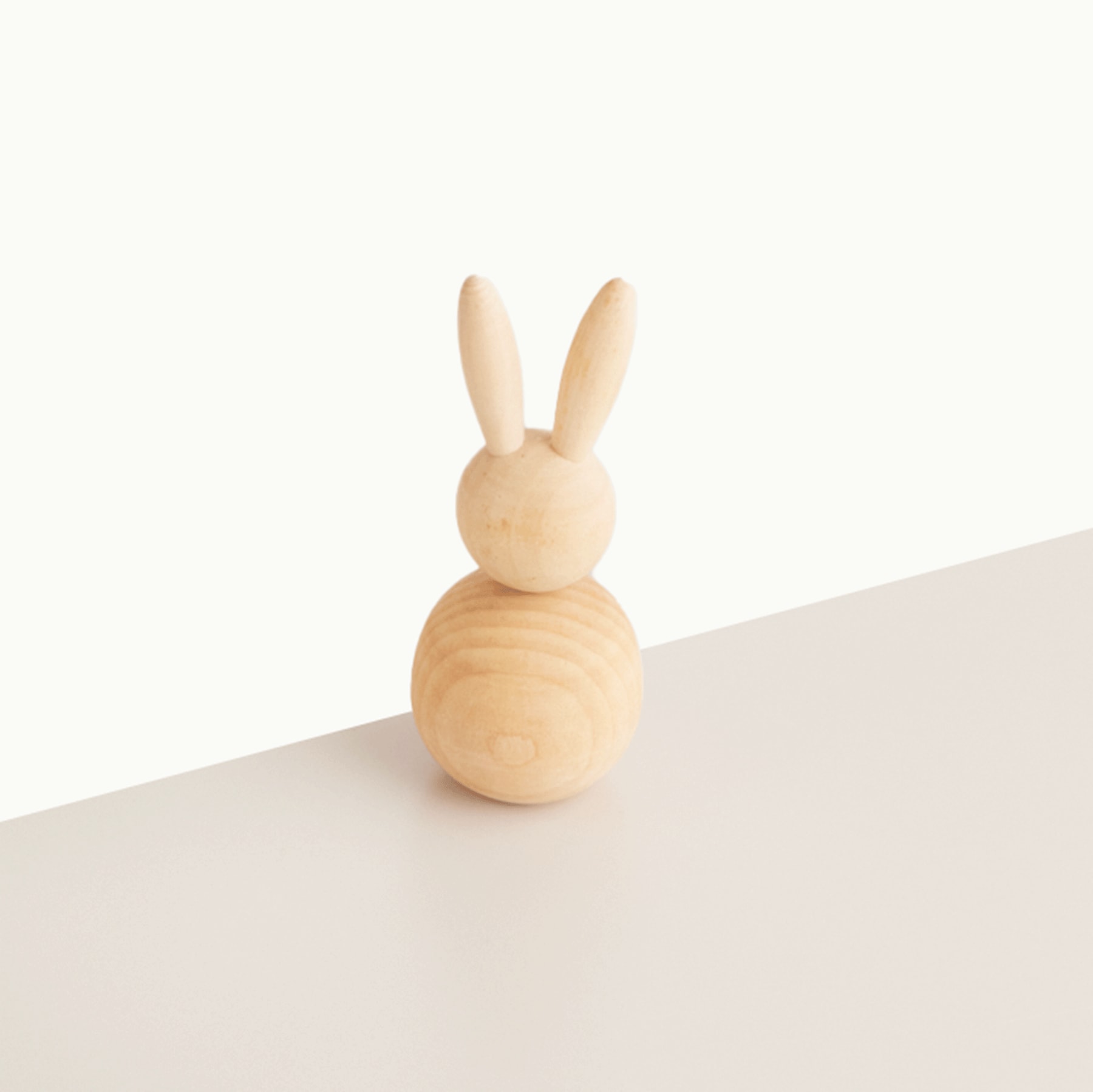Eine einfache Kaninchenfigur aus Holz sitzt auf einer schlichten weißen Oberfläche vor einem weißen Hintergrund.