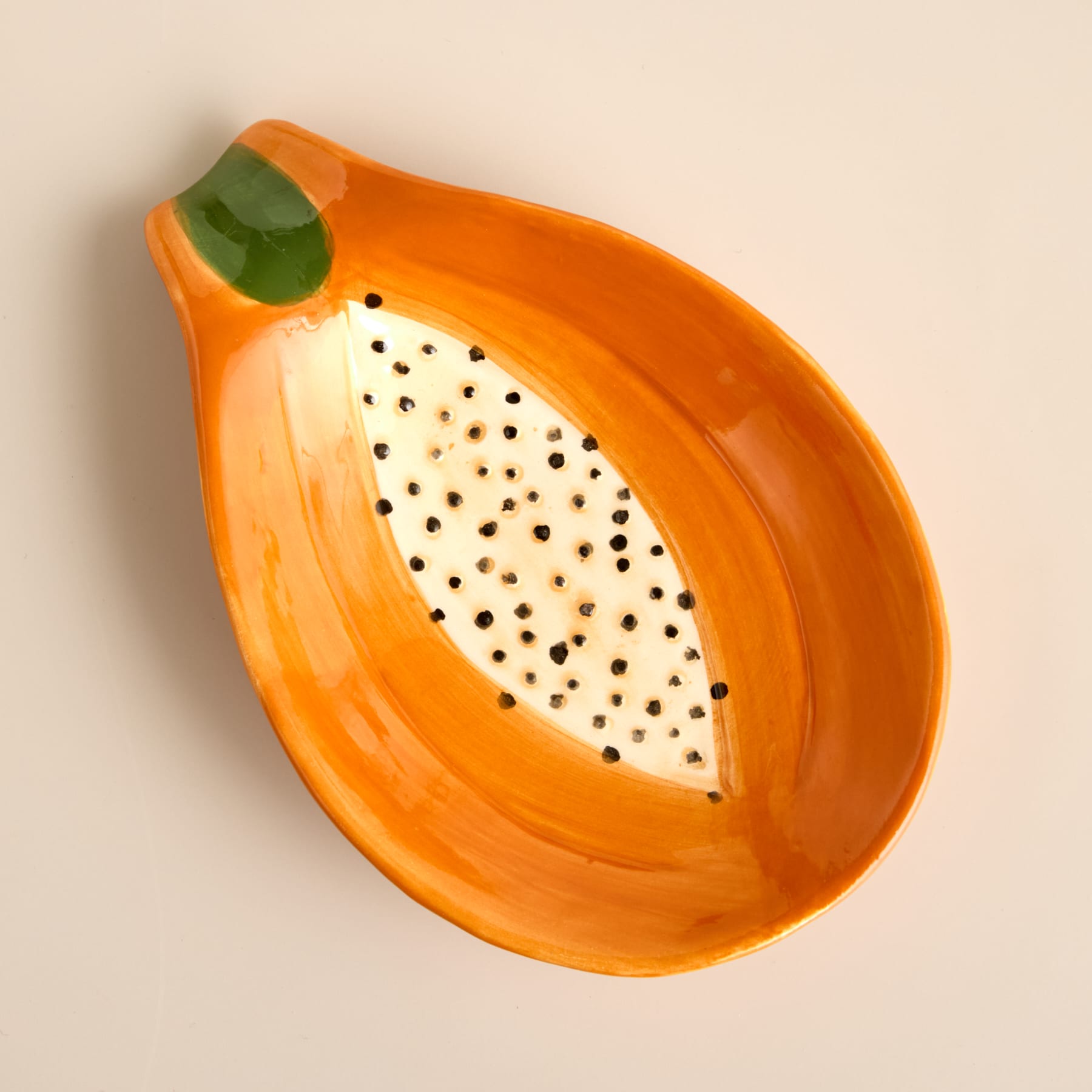 Eine leuchtend orangefarbene Keramikschale in Form einer Papaya mit einem grünen blattähnlichen Detail und einer strukturierten, gepunkteten Innenseite.