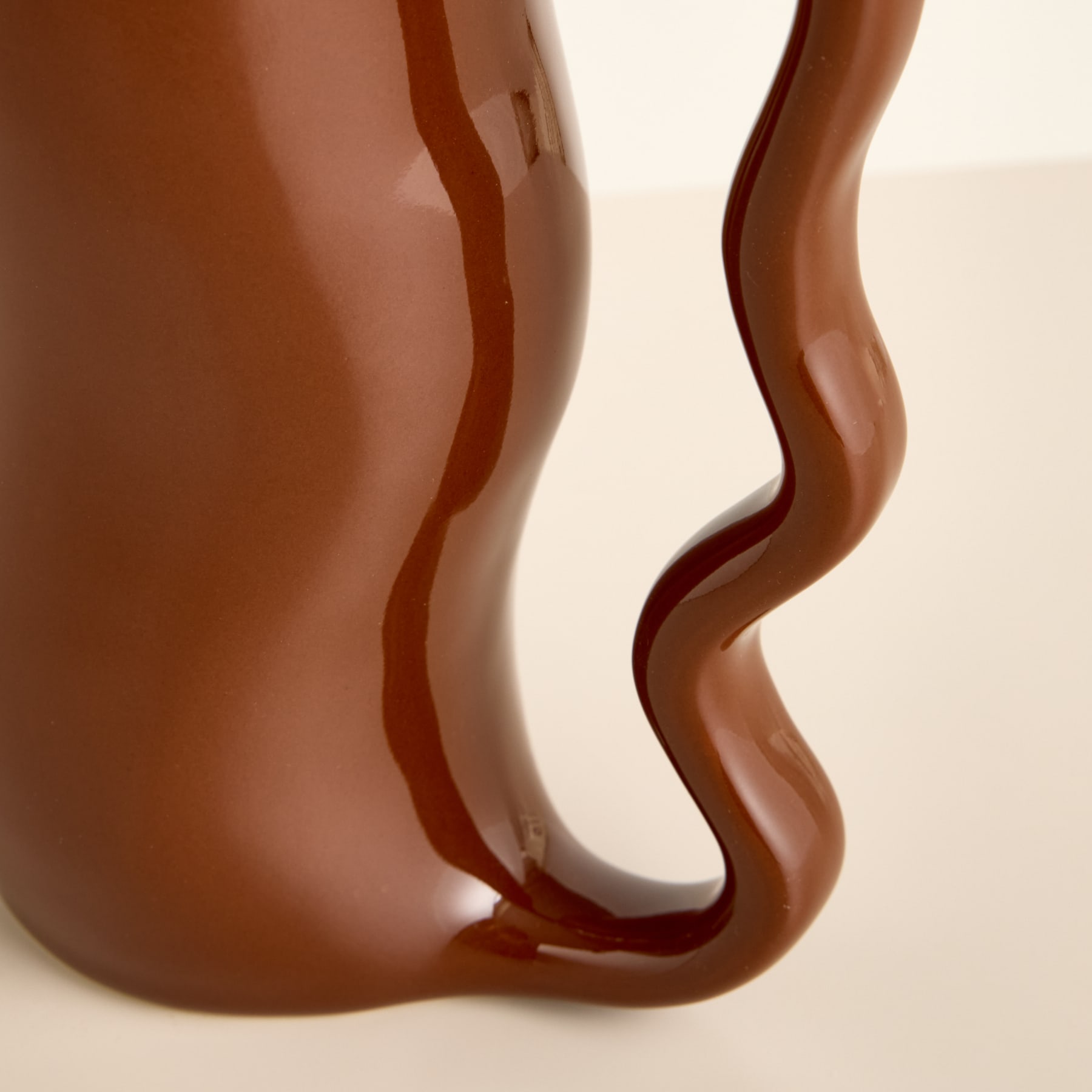 Eine braune Keramiktasse mit einem wellenförmigen, fließenden Design auf der Oberfläche vor einem schlichten, hellen Hintergrund.