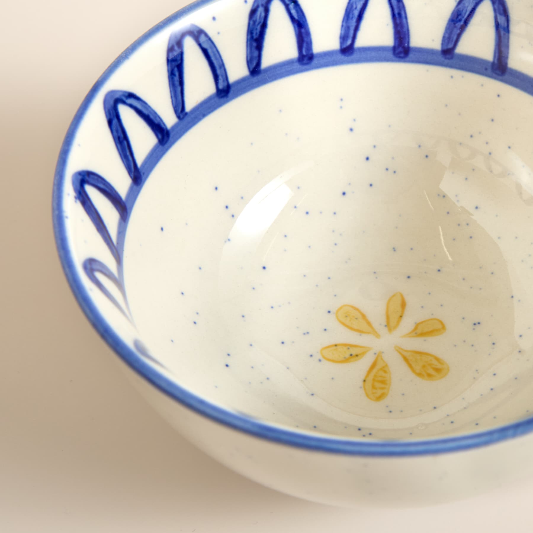 Eine weiße Keramikschüssel mit einem blauen Blumenmuster am Rand. Sie enthält eine cremefarbene Substanz, möglicherweise eine Suppe oder einen Brei, mit gelben, blumenförmigen Verzierungen, die auf der Oberfläche schwimmen.