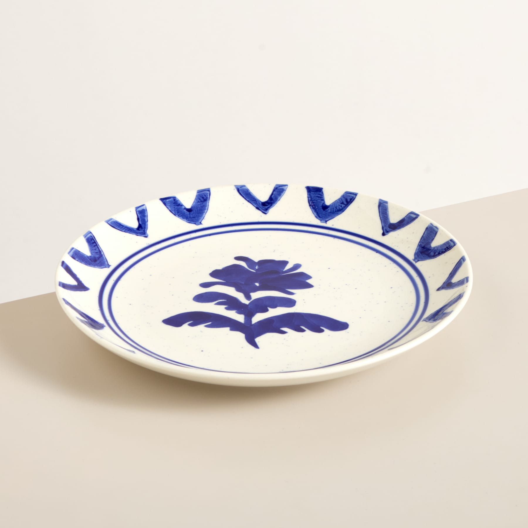 Eine weiße Keramikschale mit blauem Blumenmuster auf der Innenseite, die auf einer beigen Oberfläche ruht.