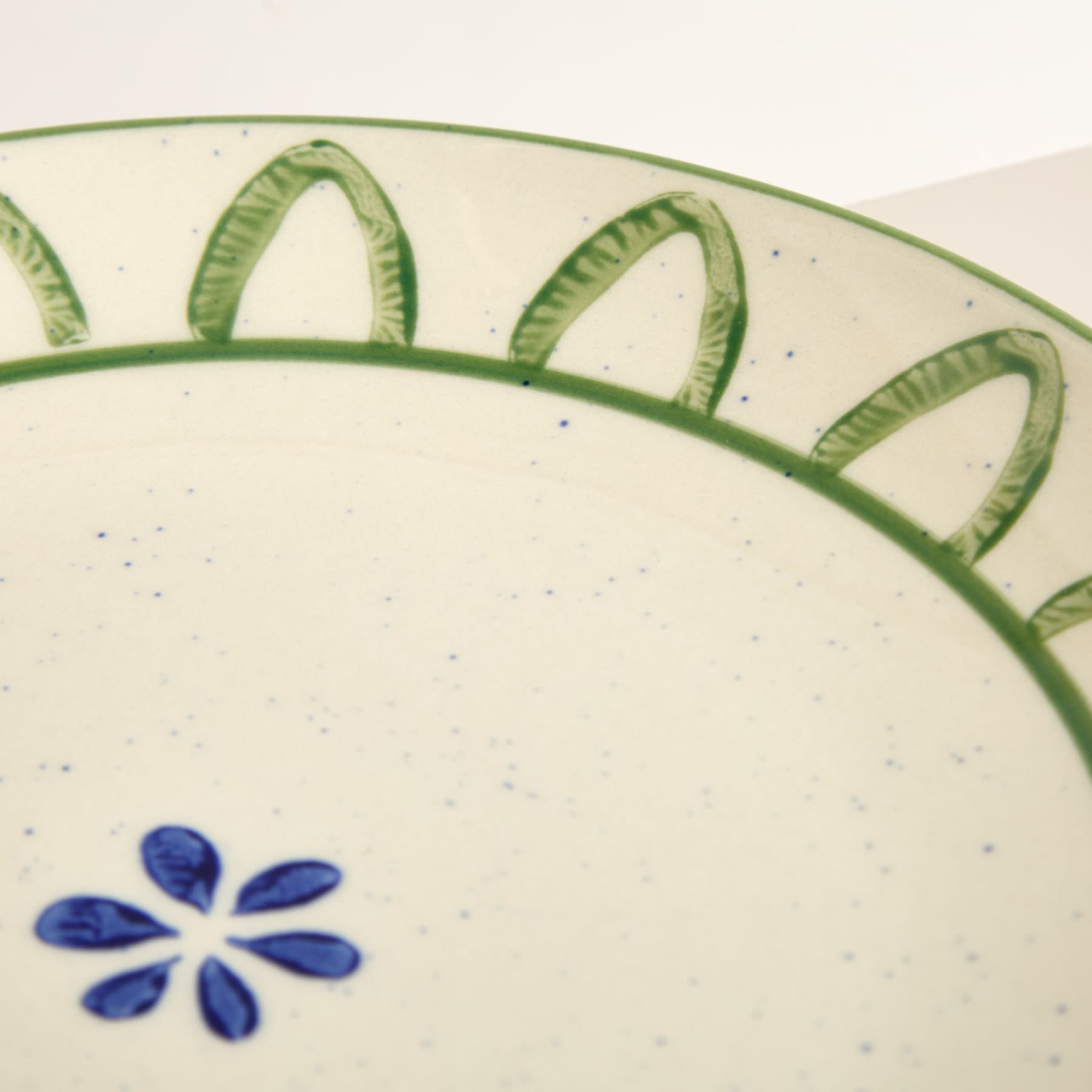 Das Bild zeigt einen Keramikteller mit einem dekorativen grünen Rand und einem blauen Blumenmuster in der Mitte.