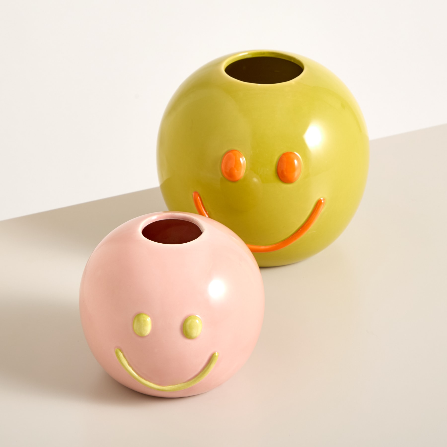 Auf einer schlichten, hellen Fläche stehen zwei bunte, kugelförmige Vasen mit lächelnden Gesichtern.