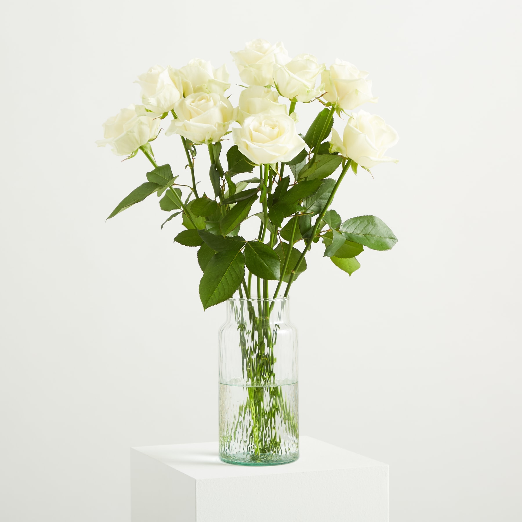 Ein Strauß wunderschöner weißer Rosen in einer Glasvase steht vor einem schlichten weißen Hintergrund.