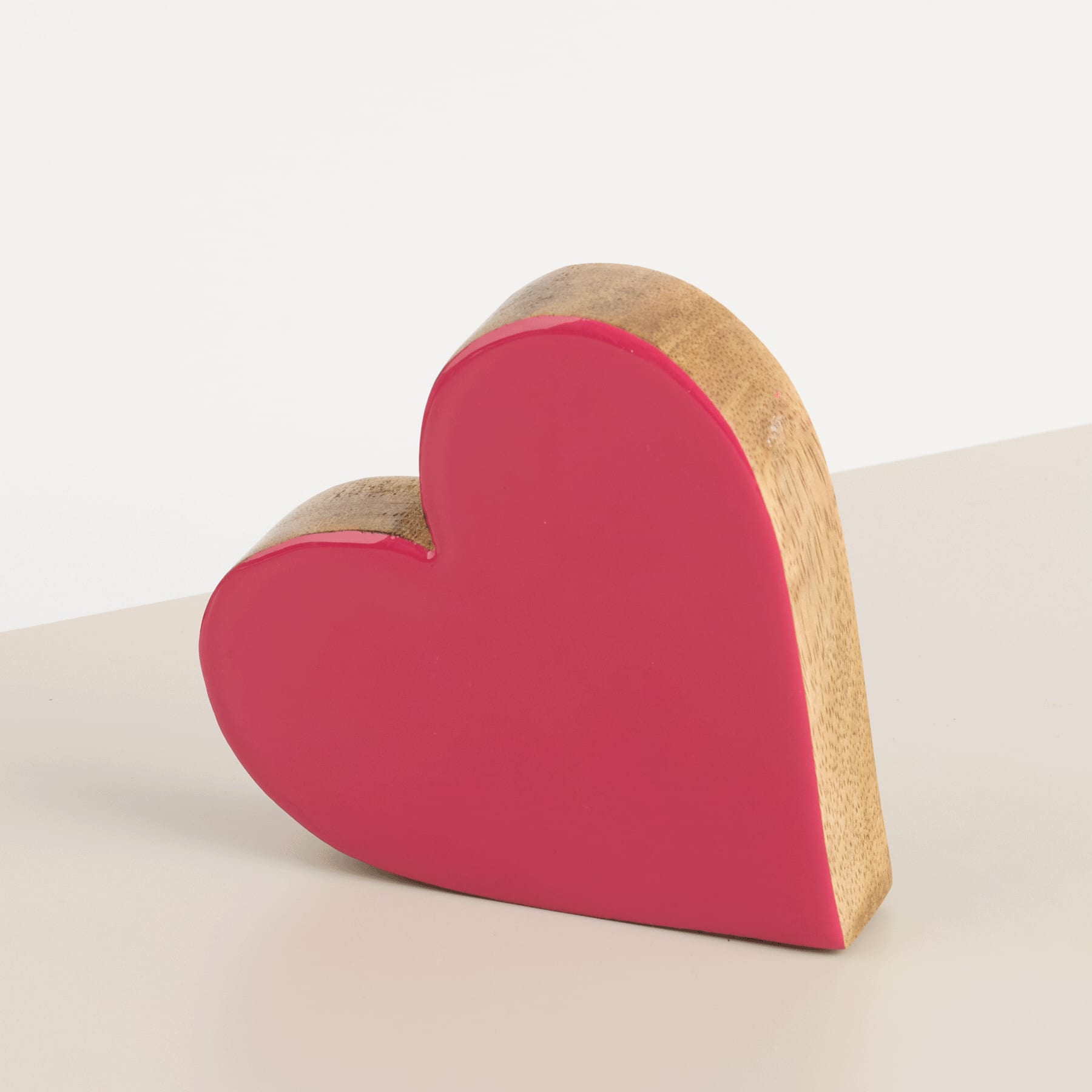 Ein rotes herzförmiges Holzobjekt liegt auf einer hellen Oberfläche vor einem schlichten Hintergrund.