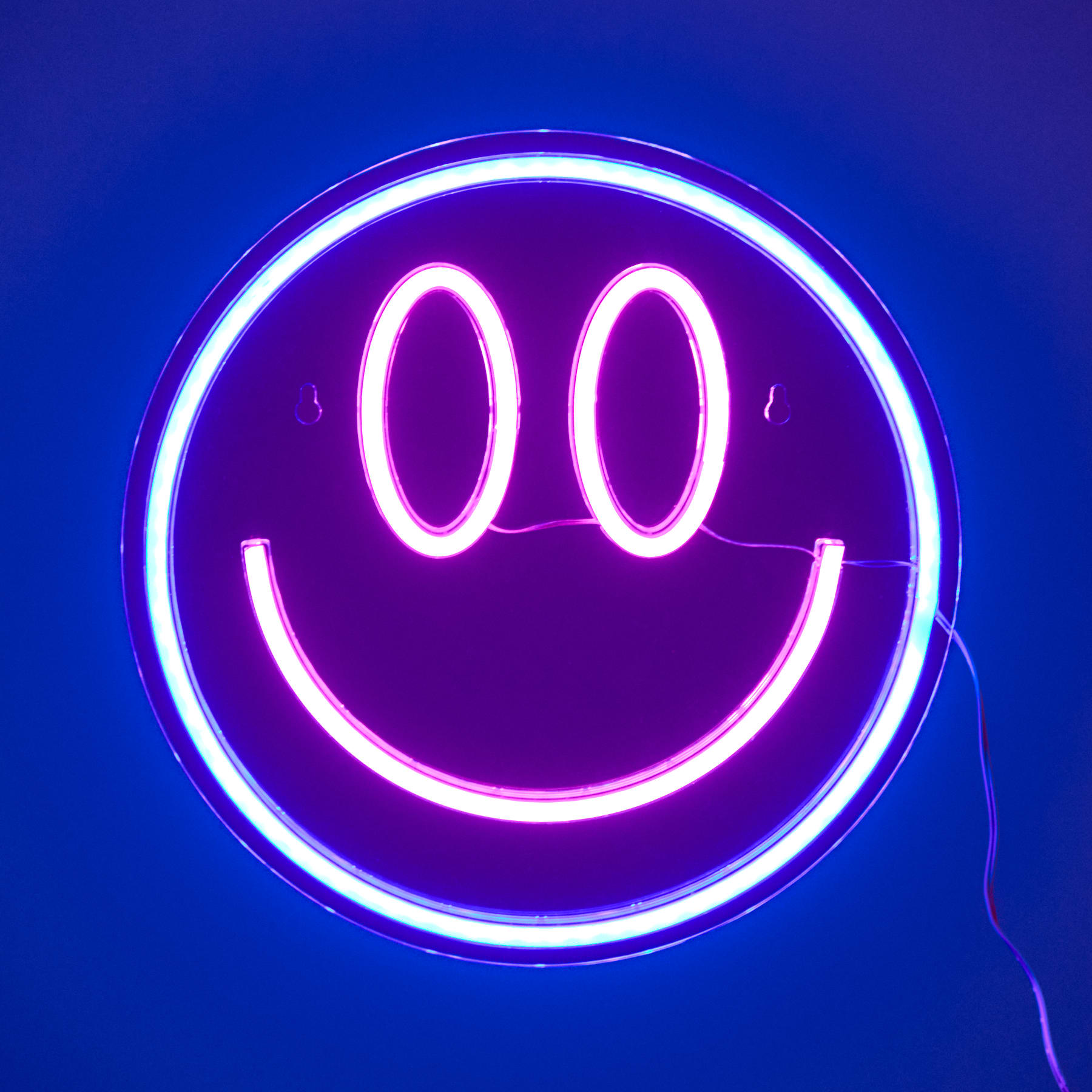 Ein leuchtendes lila Neon-Smiley-Symbol vor einem leuchtend blauen Hintergrund.