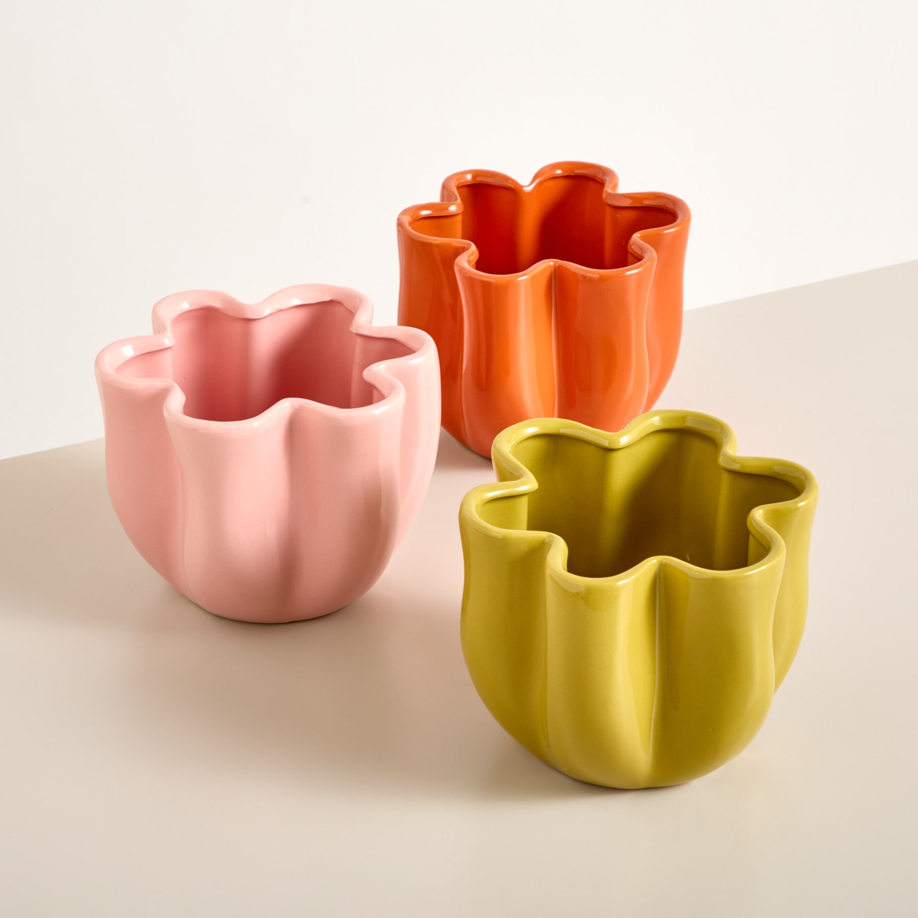 Bunte, blumenförmige Keramikbehälter in Orange-, Rosa- und Gelbtönen stehen auf einer hellen Oberfläche.