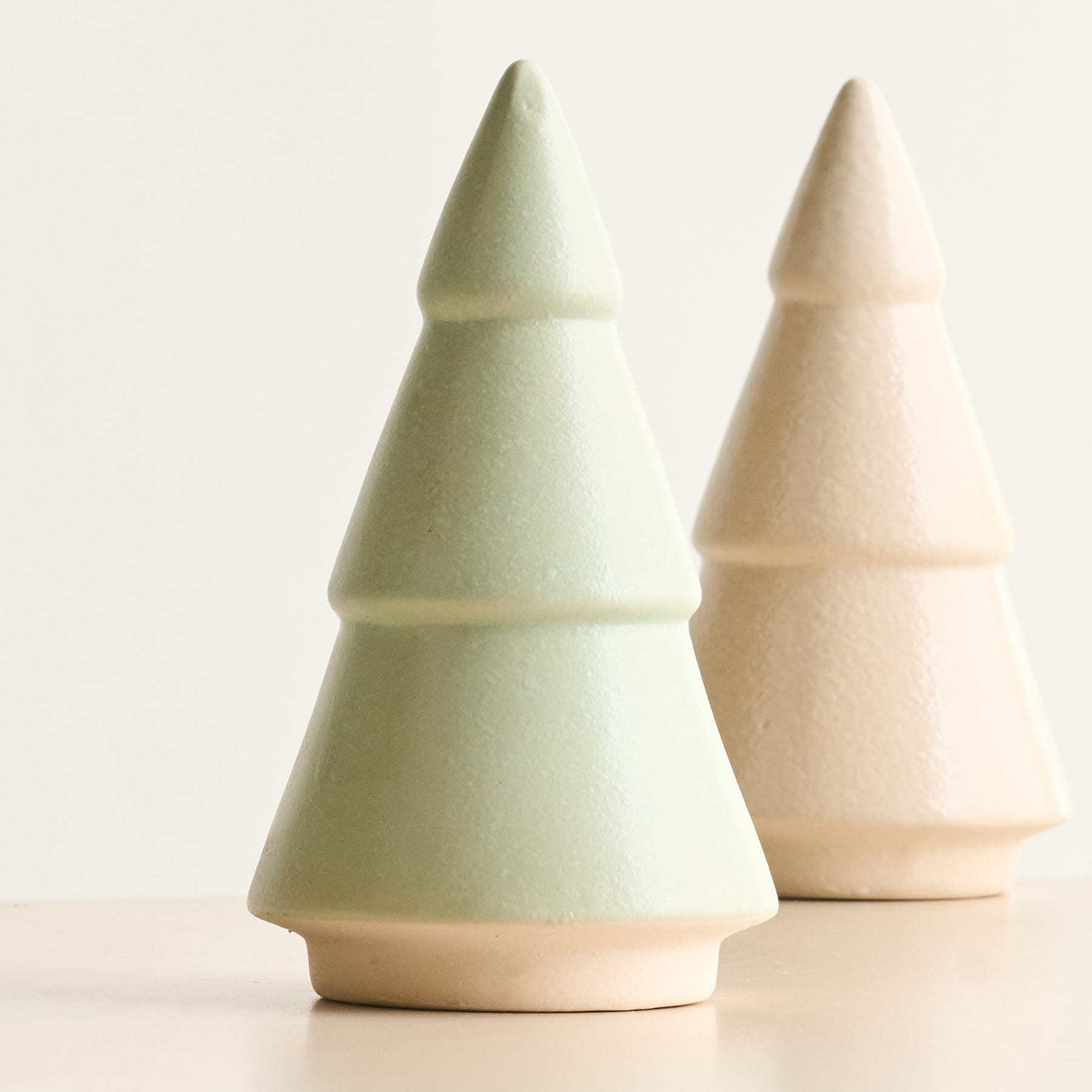 Auf einem schlichten Hintergrund stehen zwei Christbaumfiguren aus Keramik in Pastellfarben.