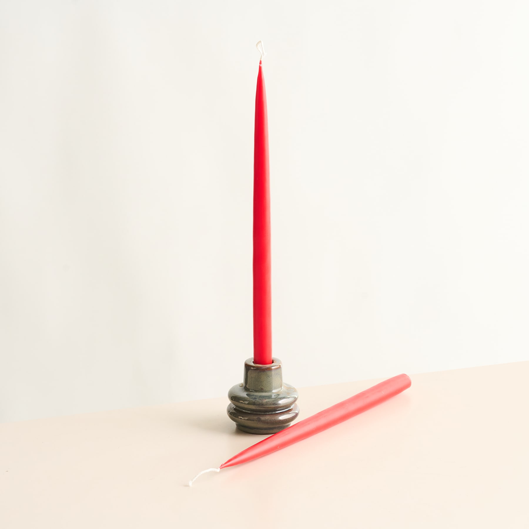 Eine leuchtend rote Kerze steht aufrecht auf einer Holzoberfläche mit einem schlichten weißen Hintergrund.