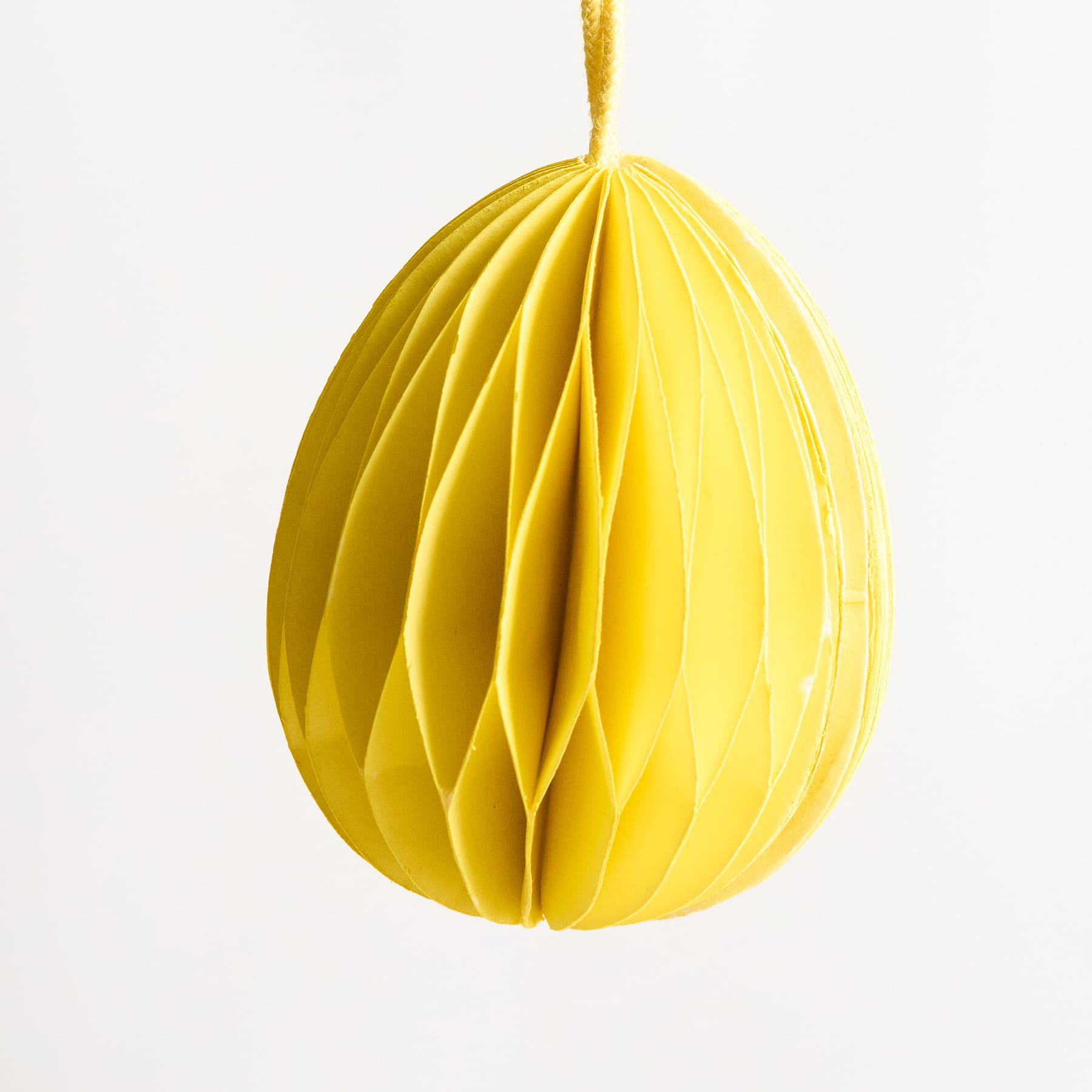 Eine leuchtend gelbe, wabenartige Struktur hängt vor einem schlichten weißen Hintergrund und erzeugt einen auffälligen visuellen Kontrast.