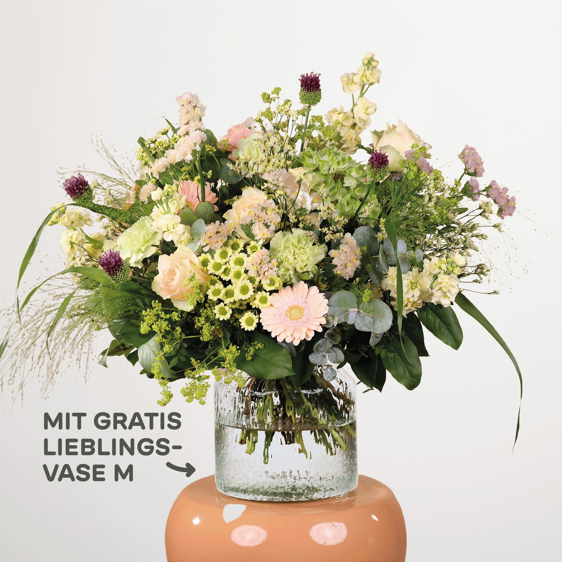 Ein farbenfroher Strauß verschiedener Blumen, darunter Chrysanthemen, Gänseblümchen und Grünpflanzen, wird in einer Glasvase auf einem Sockel präsentiert, mit einem Schild, das auf ein Sonderangebot für eine „Lieblingsvase“ hinweist.