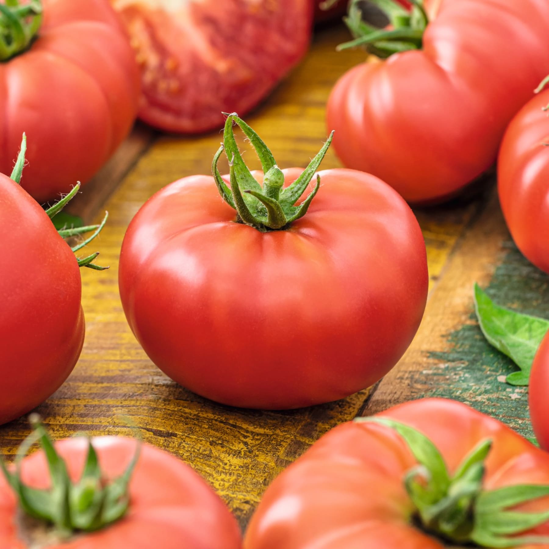 Leuchtend rote Tomaten liegen auf einer Holzoberfläche, umgeben von üppigen grünen Blättern, und bilden so eine optisch ansprechende und appetitliche Präsentation.